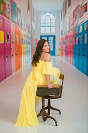 Young woman in a yellow dress sitting on a wooden chair in a colorful hallway.