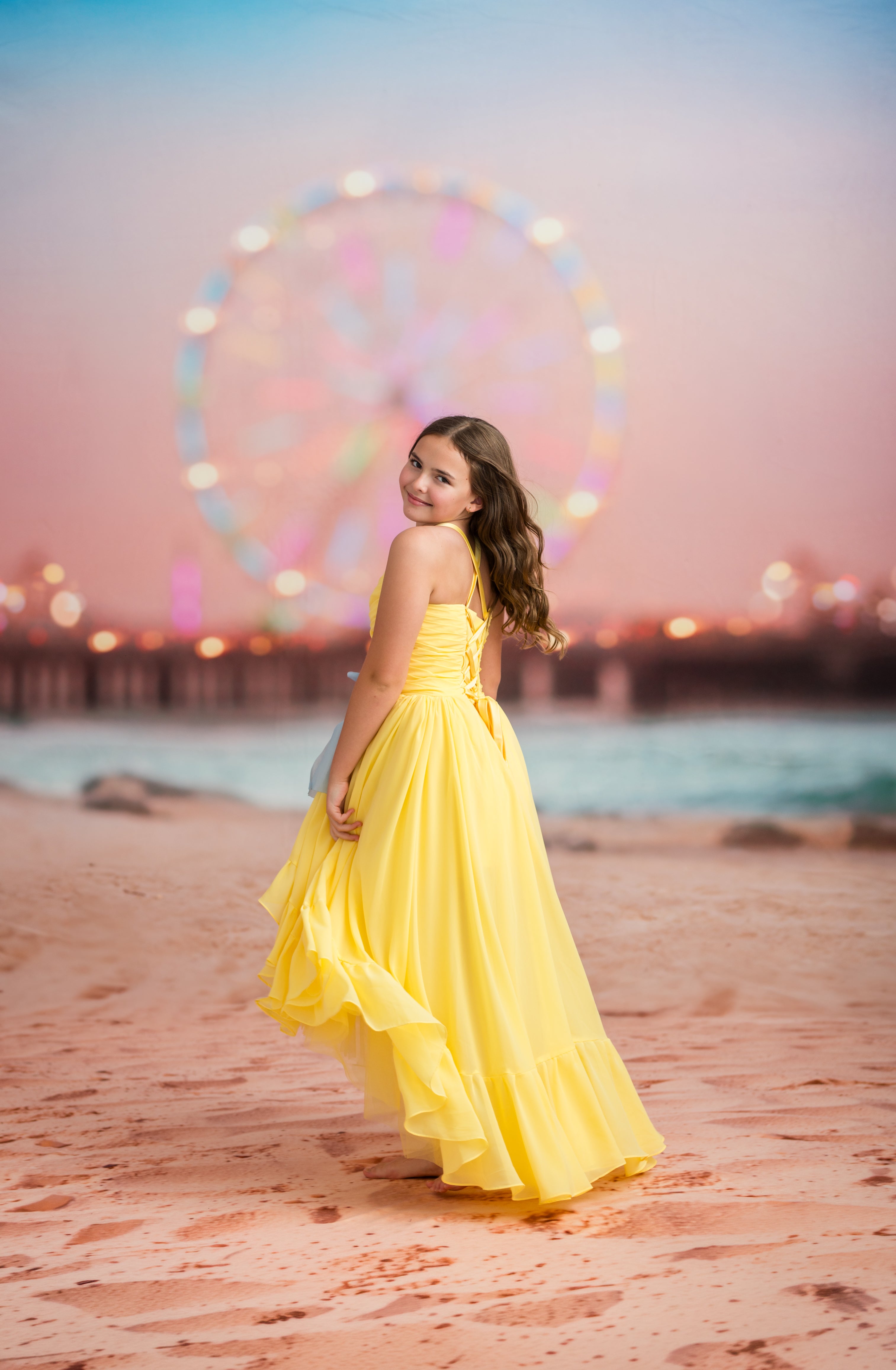 Woman in a yellow dress standing on a beach with a Ferris wheel in the background