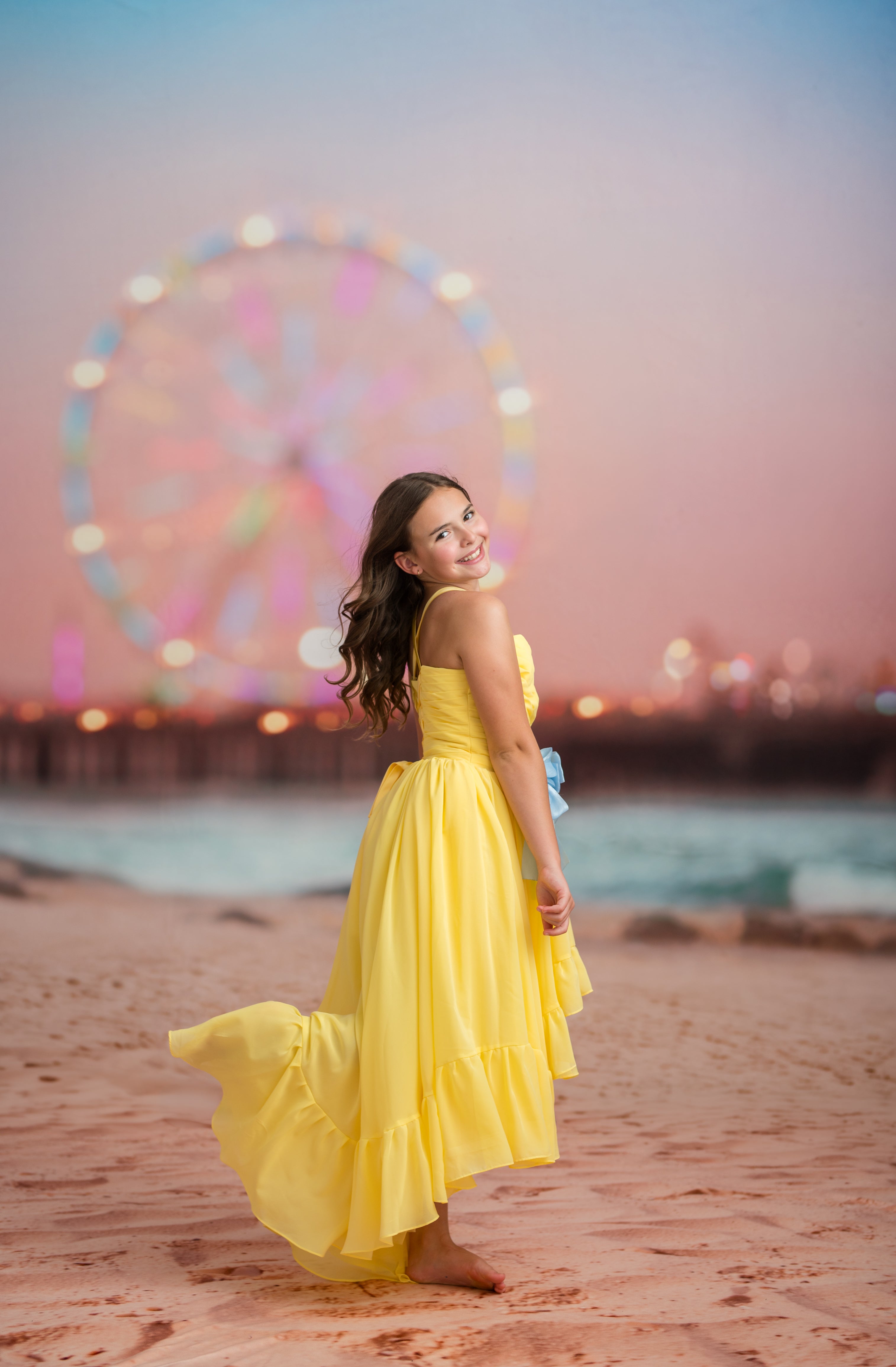 Woman in a yellow dress standing on a beach with a Ferris wheel in the background