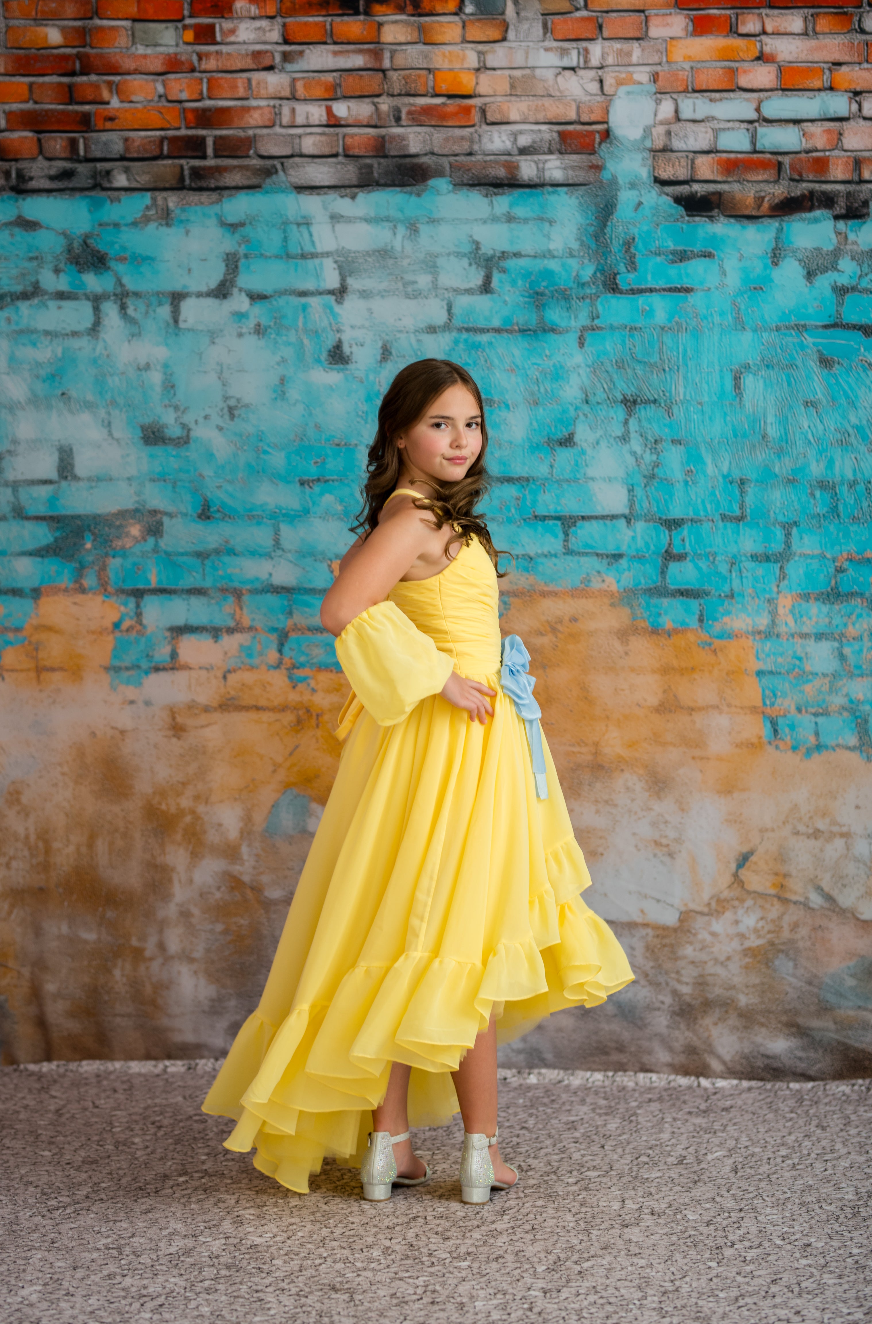 Woman in a yellow dress standing against a textured wall with blue and brown colors.