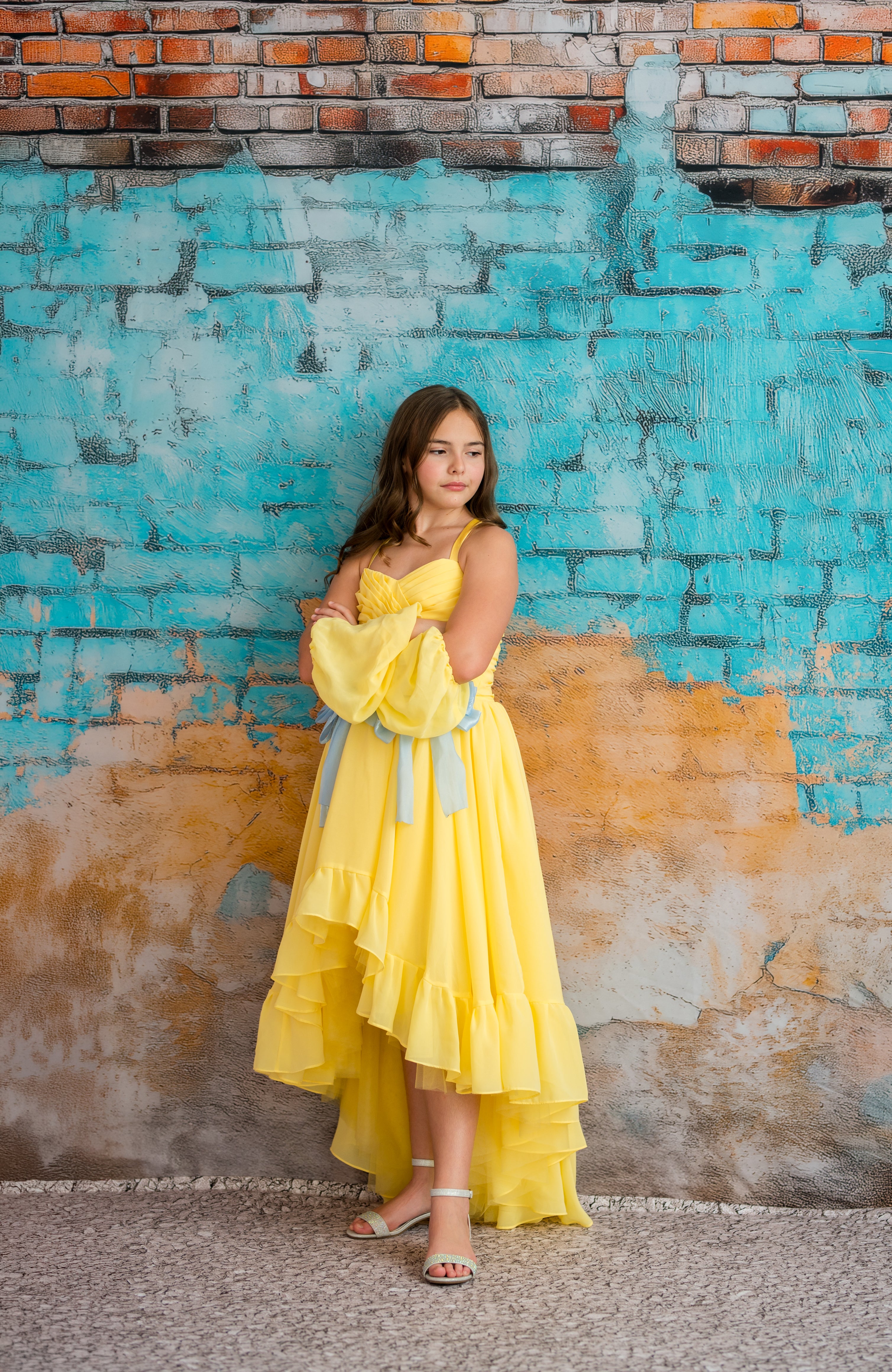Woman in a yellow dress standing against a textured wall with blue and brown colors.