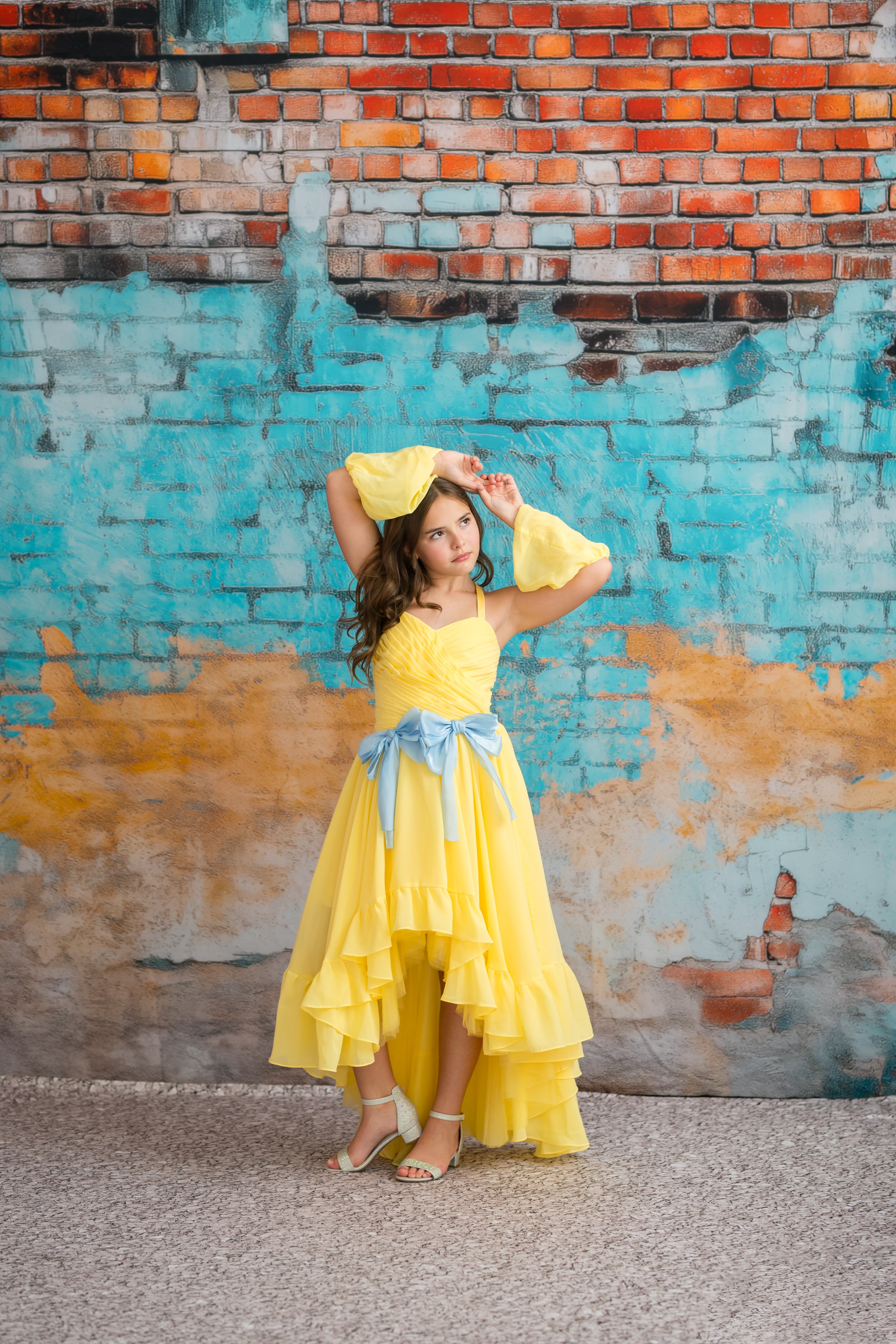 Woman in a yellow dress posing against a colorful brick wall.