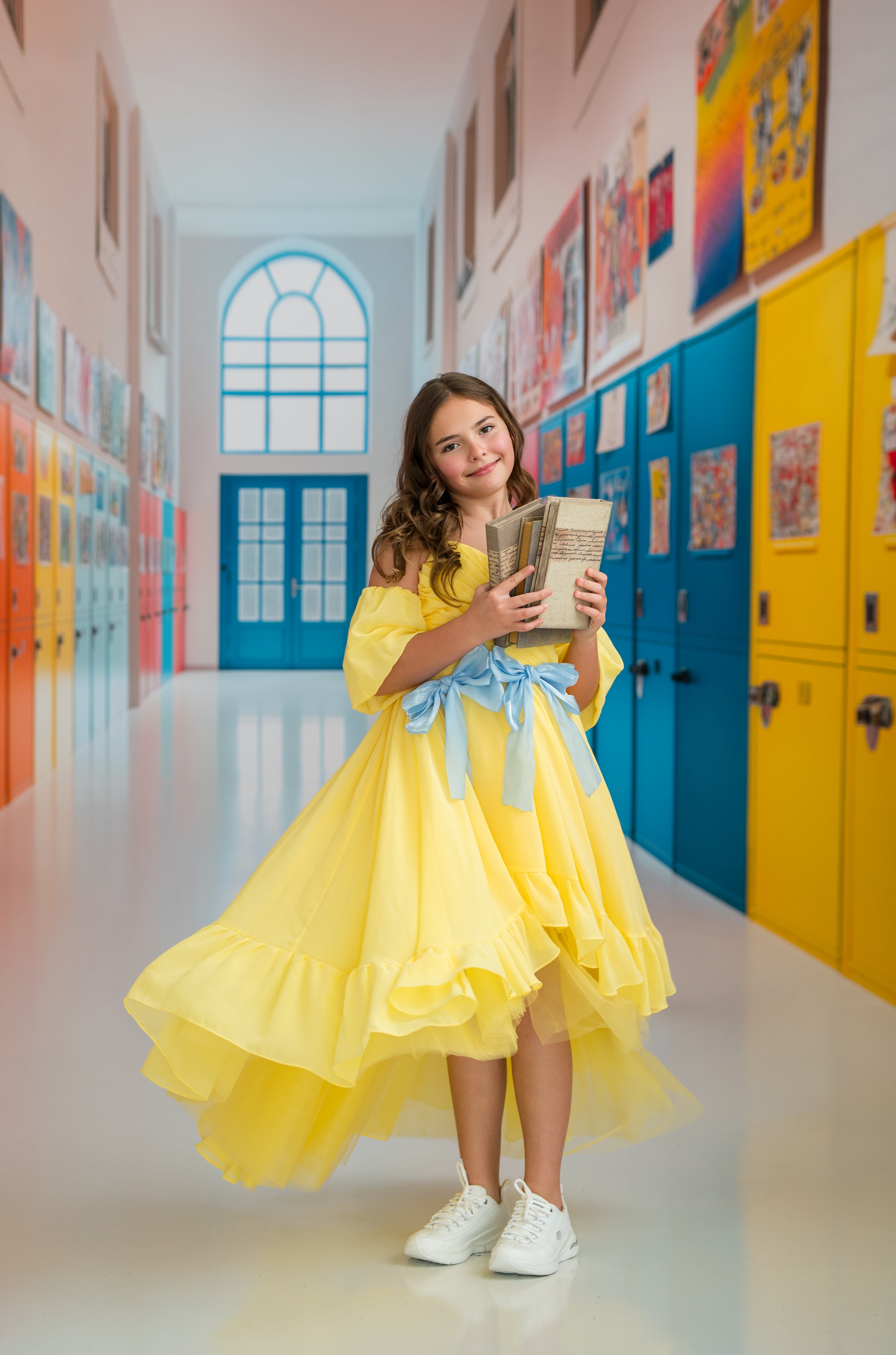 Young girl in a yellow dress holding a book in a colorful school hallway.