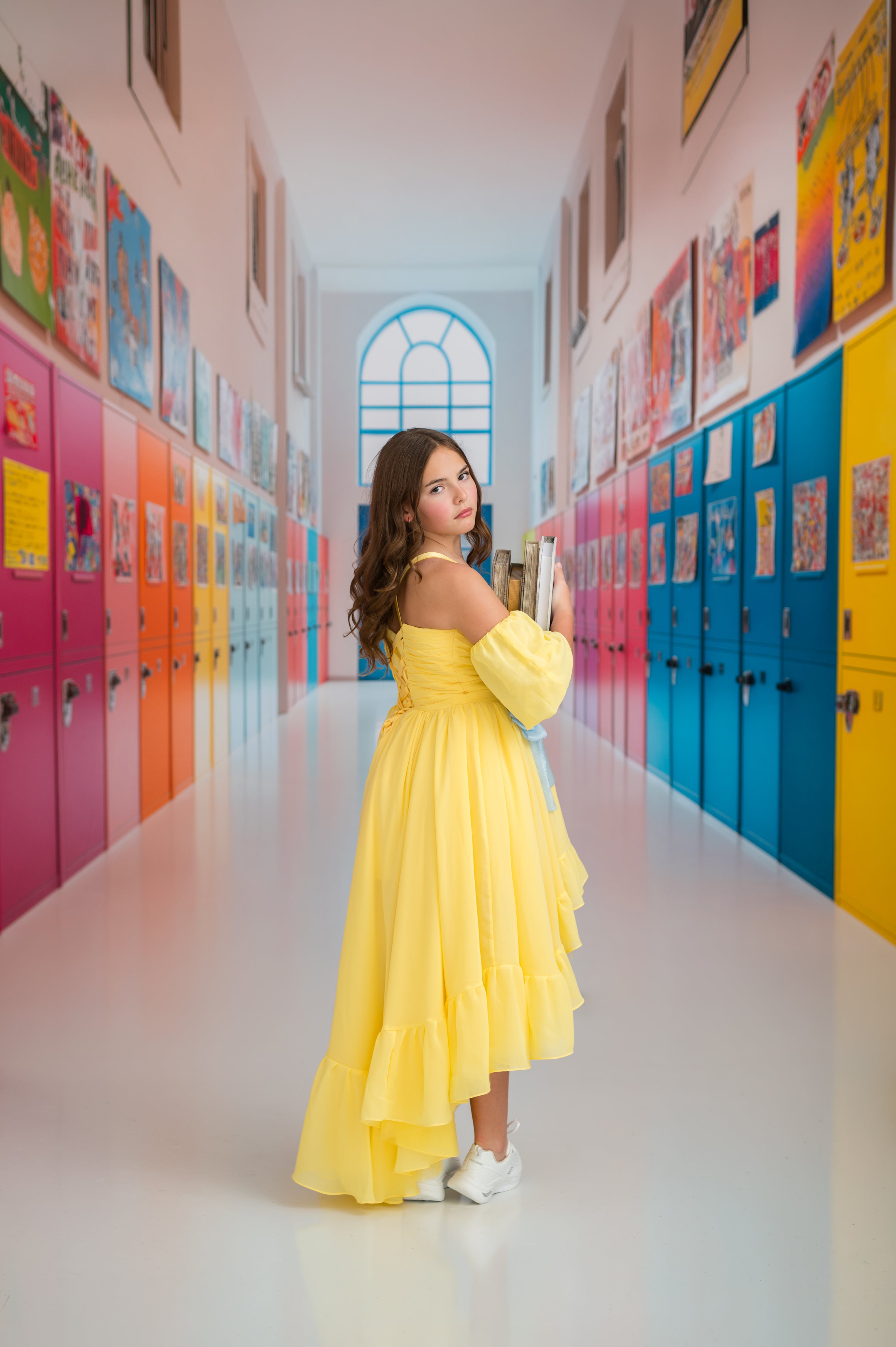 Woman in a yellow dress standing in a colorful hallway with lockers.