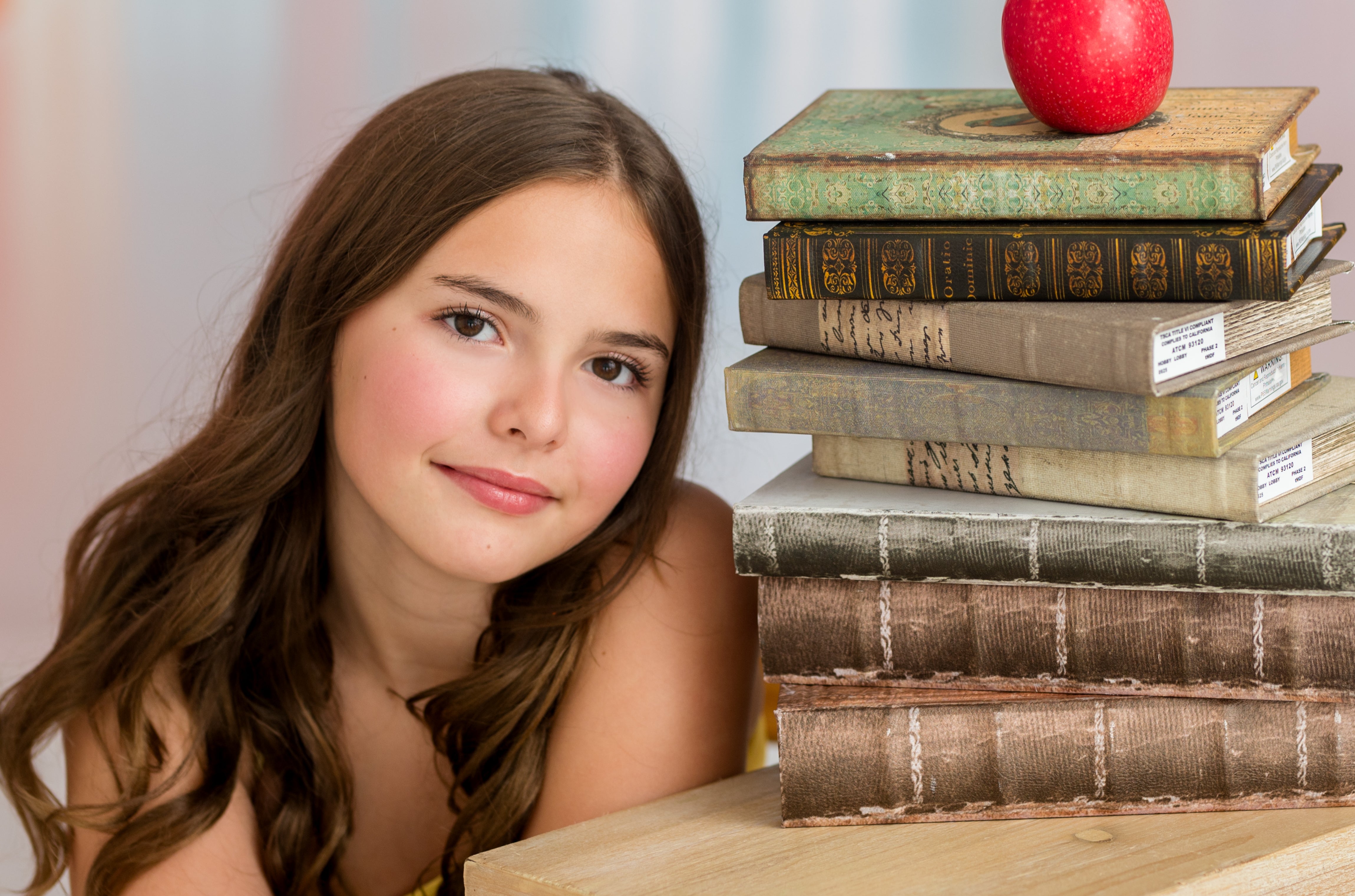 Young girl leaning on a stack of books with an apple on top, against a light background