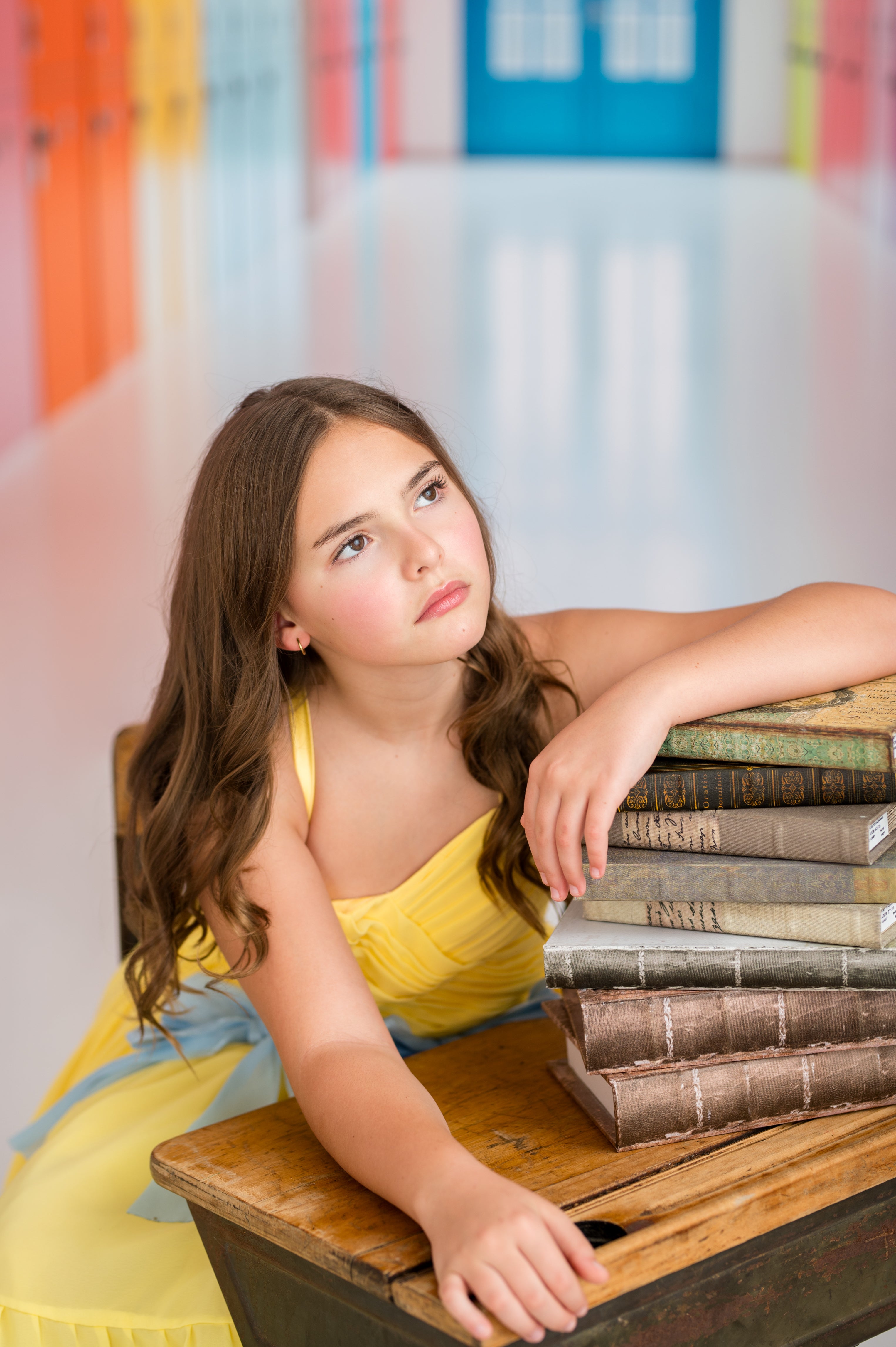 Young girl in a yellow dress sitting at a desk with books, in a classroom setting.