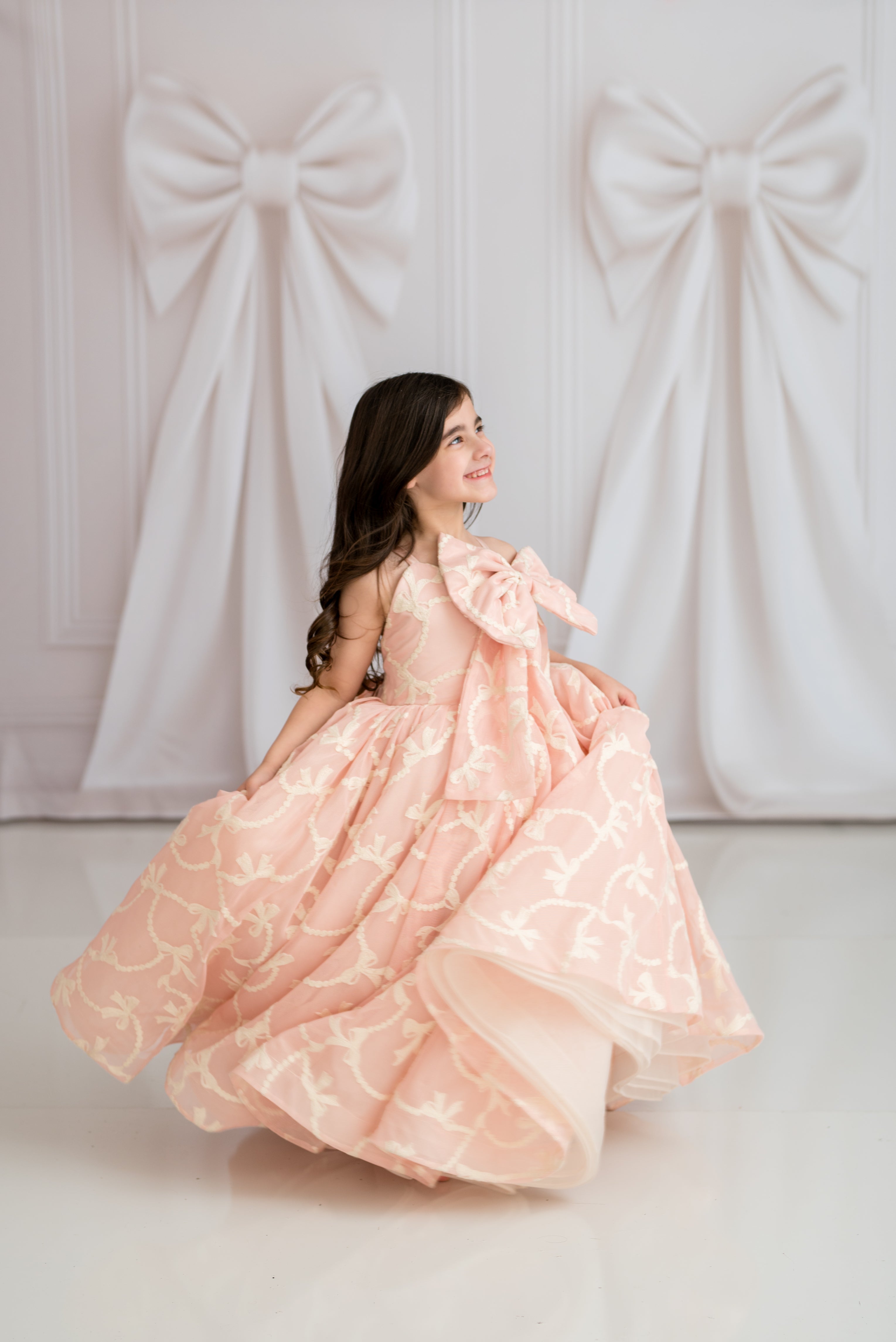 Woman in a pink gown standing against a backdrop with large bows.