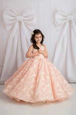 Young girl in a pink floral dress standing against a white wall with large decorative bows.