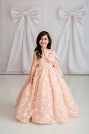 Young girl in a pink floral dress standing against a white wall with decorative bows.