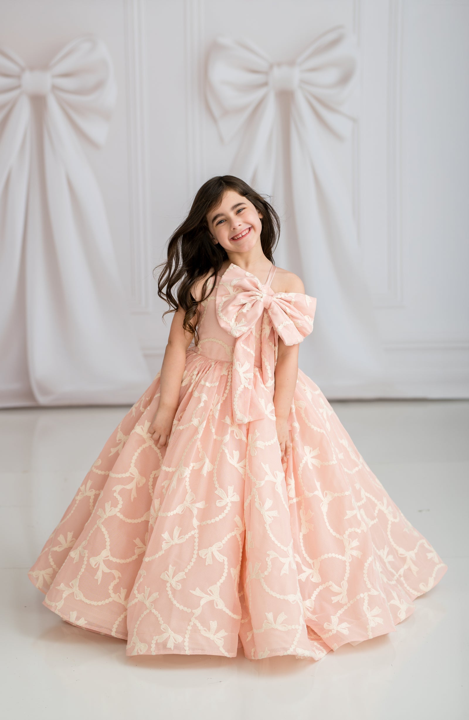 Young girl in a pink floral dress with a large bow standing against a white background