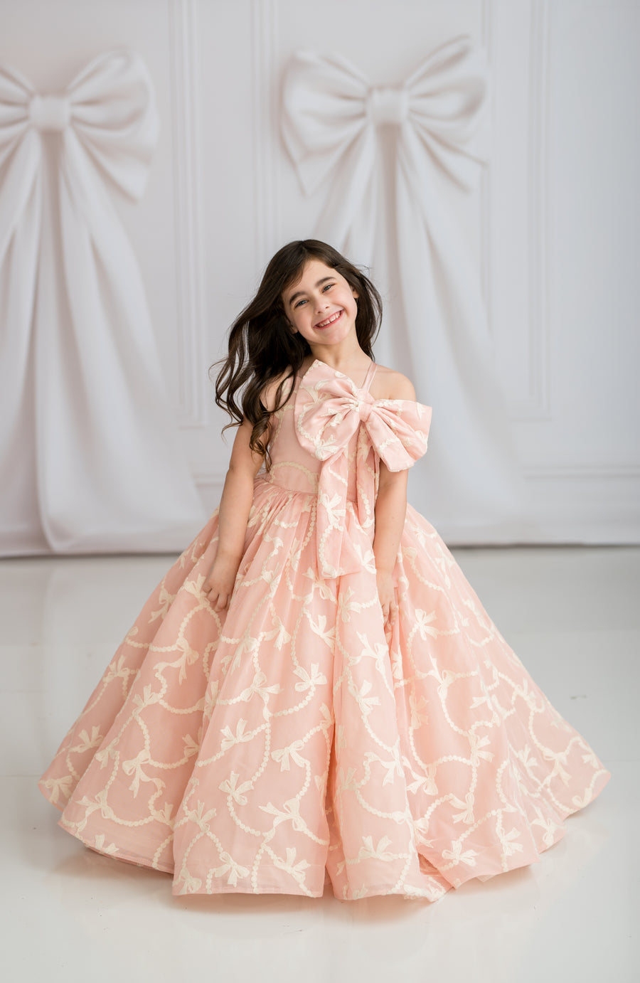 Young girl in a pink floral dress with a large bow standing against a white background