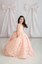 Young girl in a pink floral dress standing against a white background with large decorative bows.