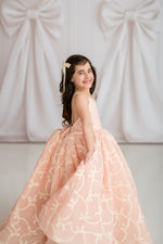 Young girl in a pink floral dress standing against a white curtain backdrop