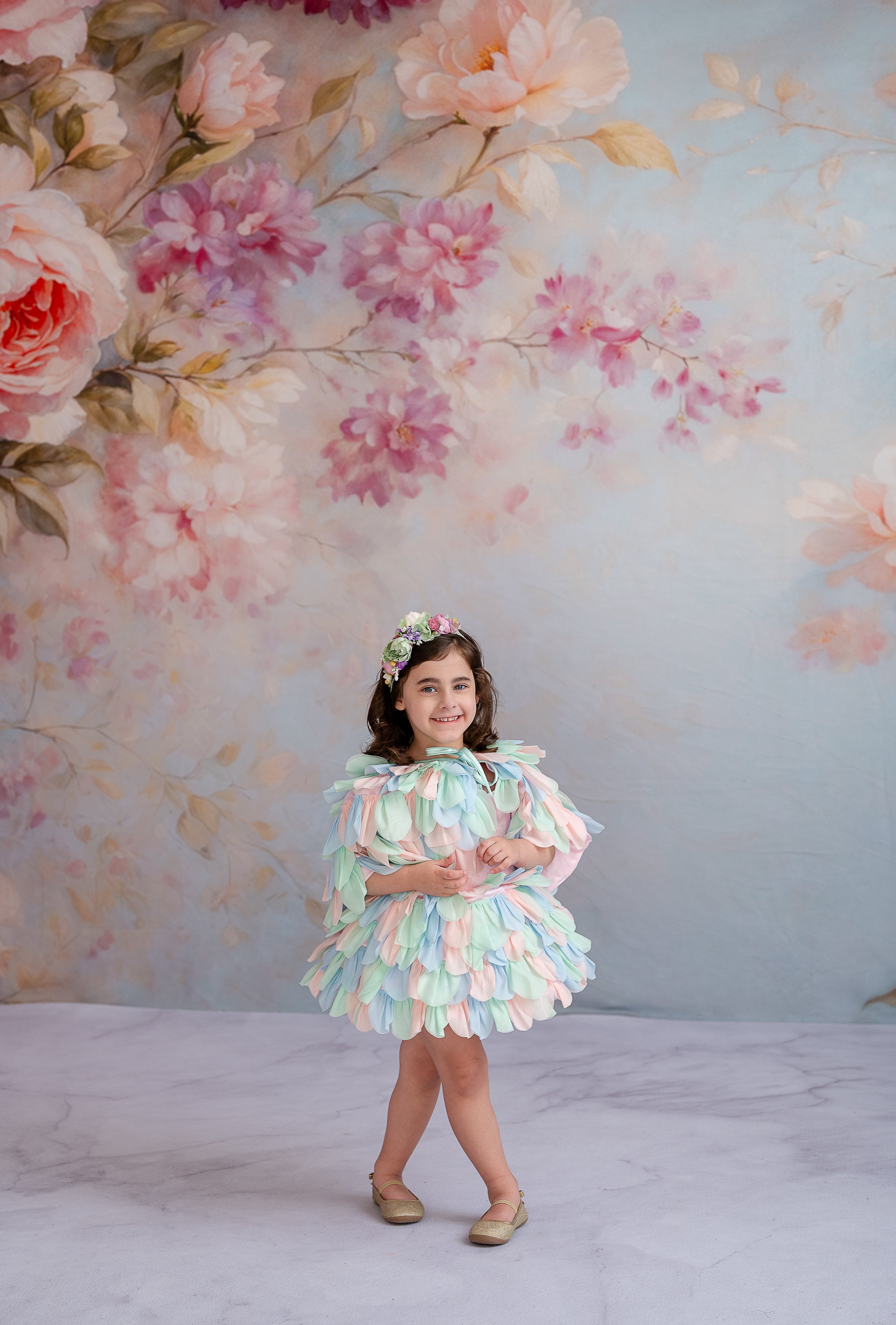 "Young girl in a pastel petal dress poses gracefully against a floral backdrop."
