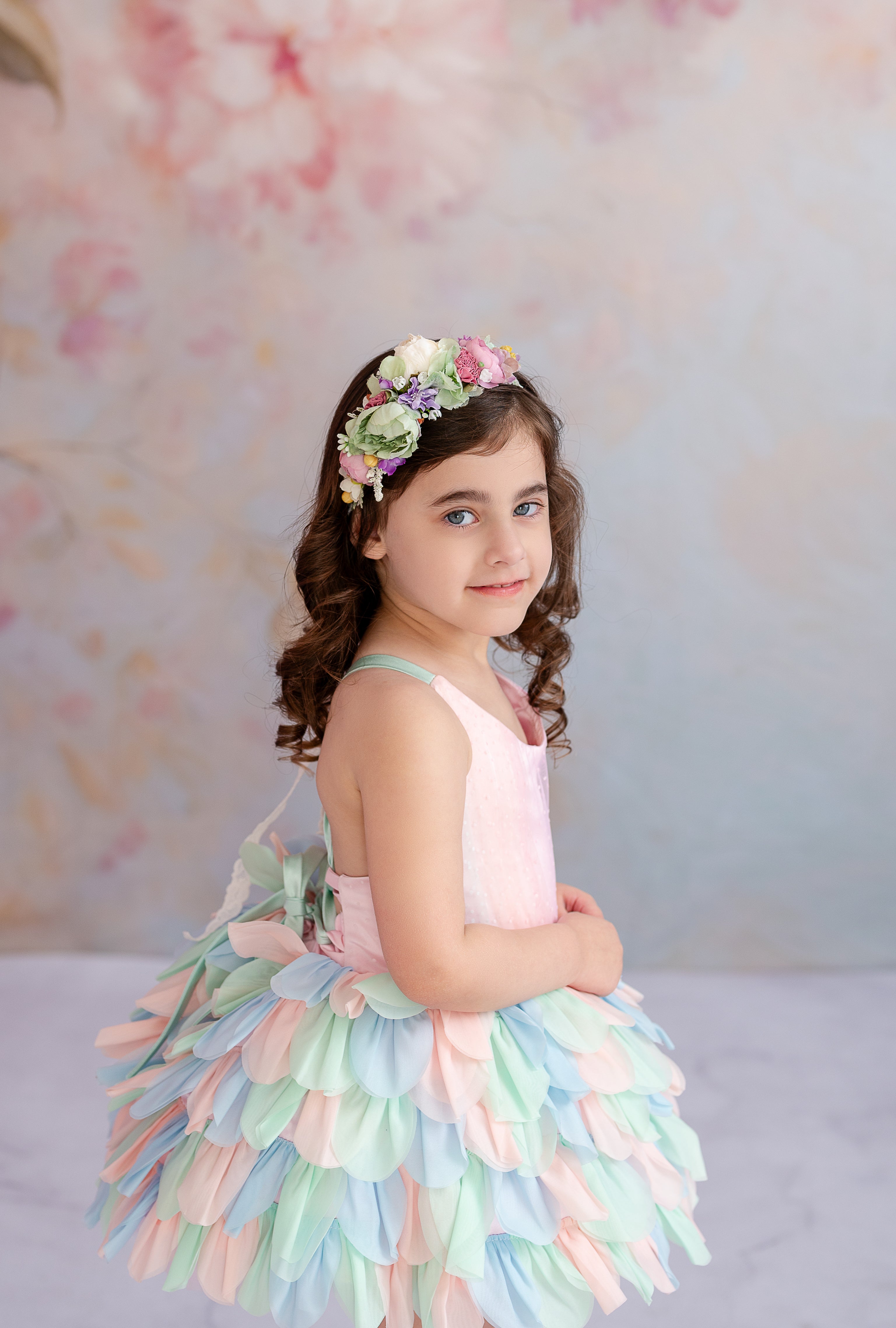 "Child wearing a colorful layered petal gown with a matching floral headpiece."
