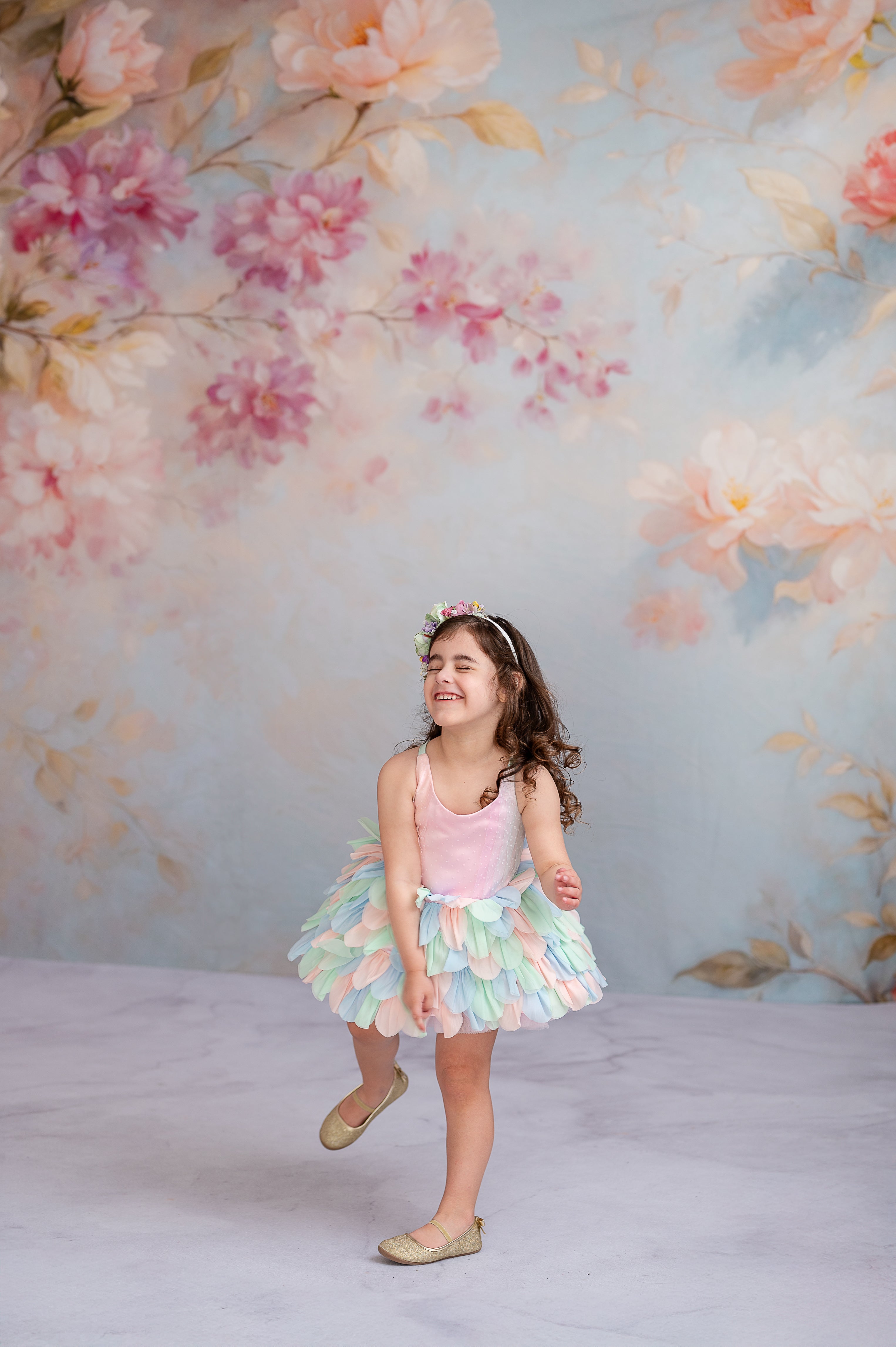 "A young model in a designer petal dress strikes a charming pose in a floral studio setting."
