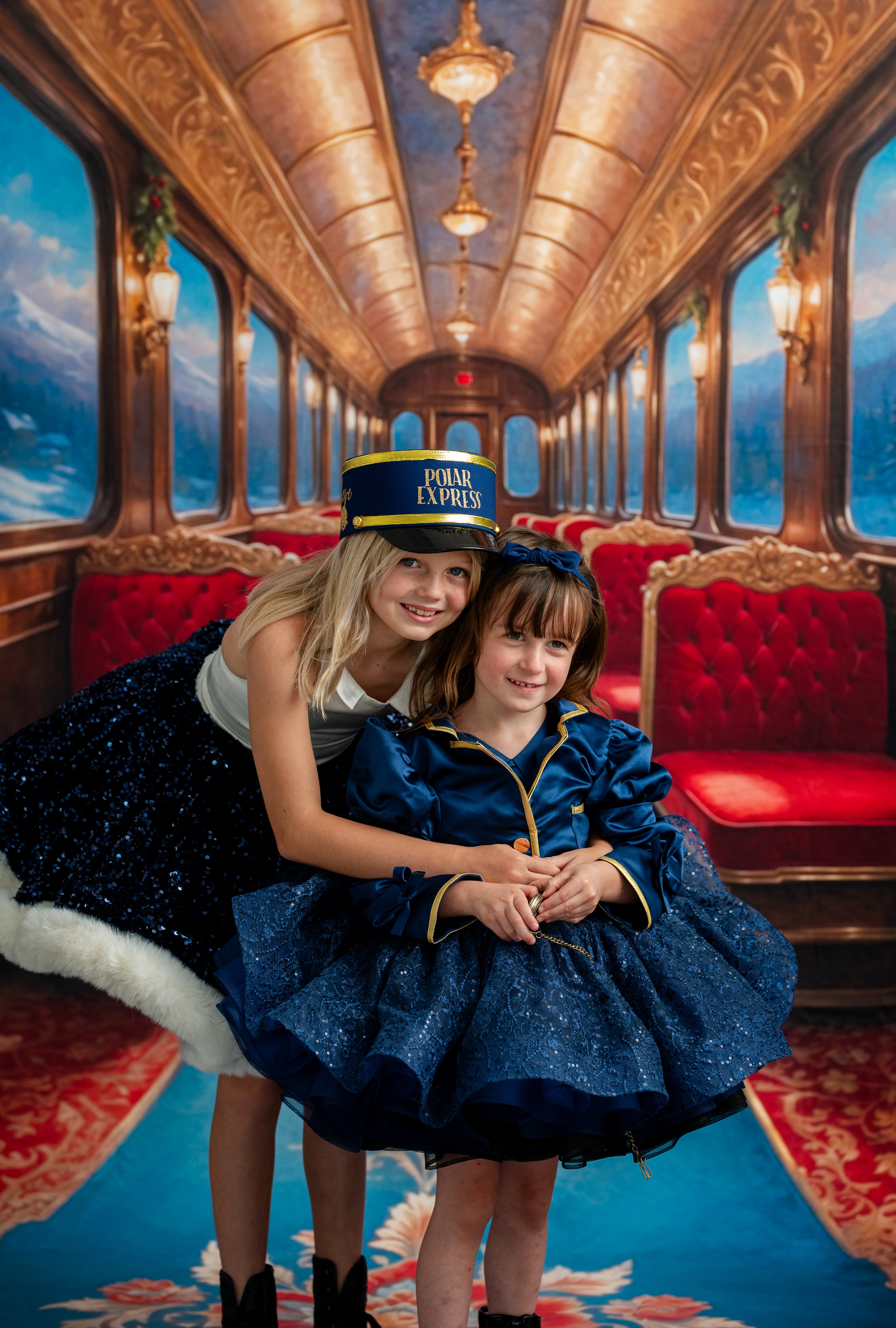 Two women in formal attire on a luxurious train car with red seats and ornate ceiling.
