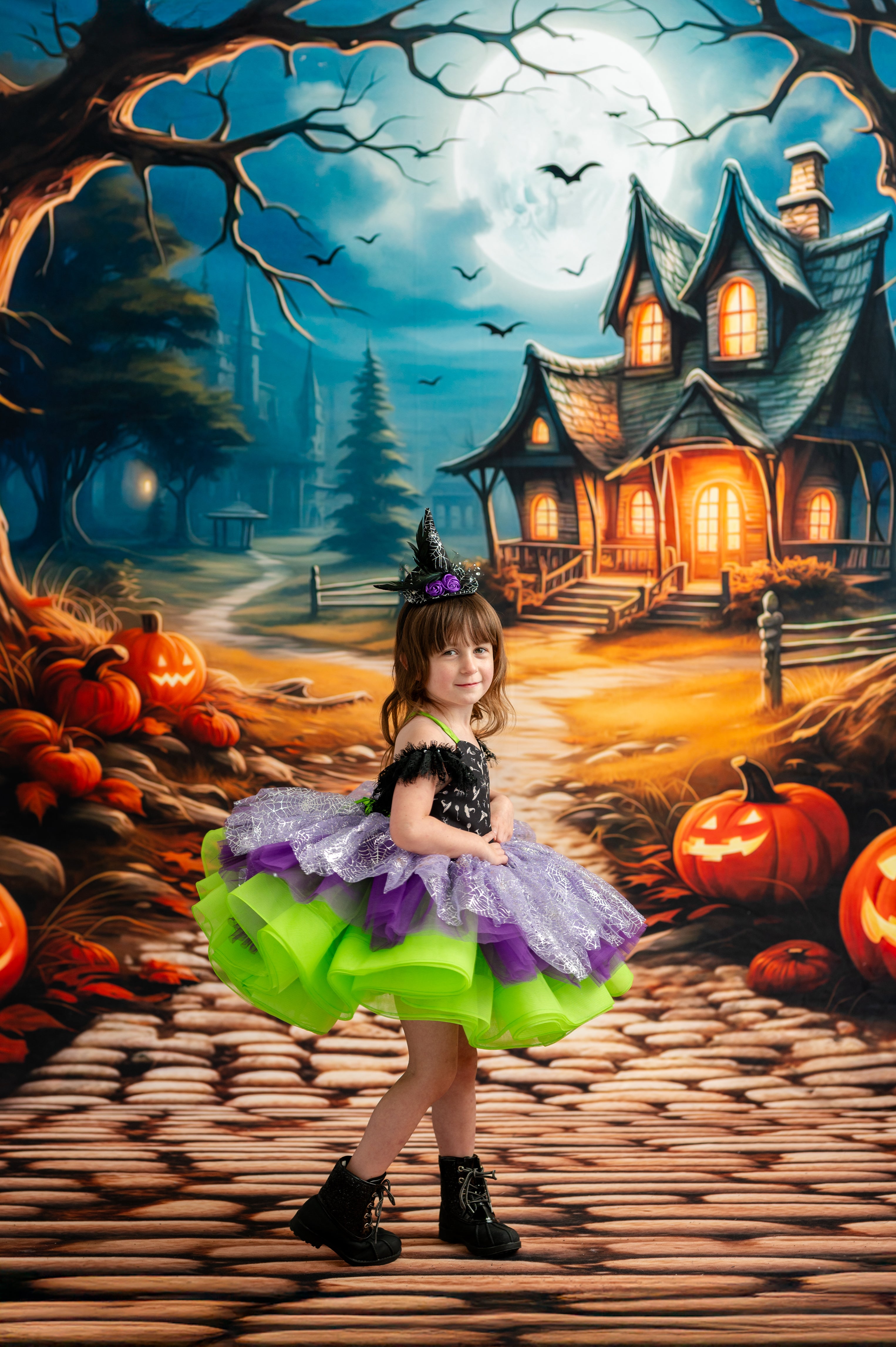 Child in a Halloween-themed dress standing in front of a haunted house and pumpkins.