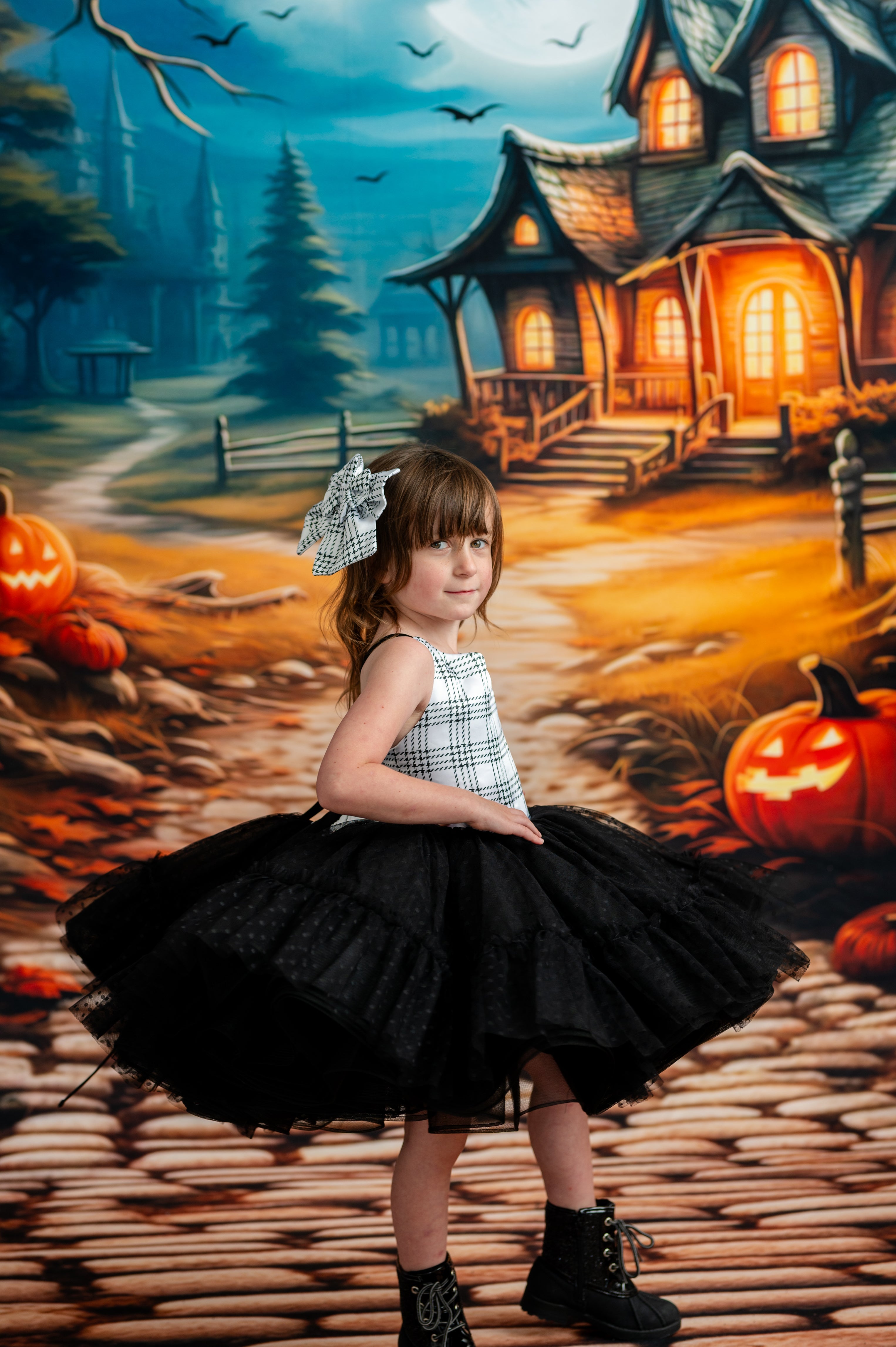 Child in a Halloween-themed setting with pumpkins and a haunted house.