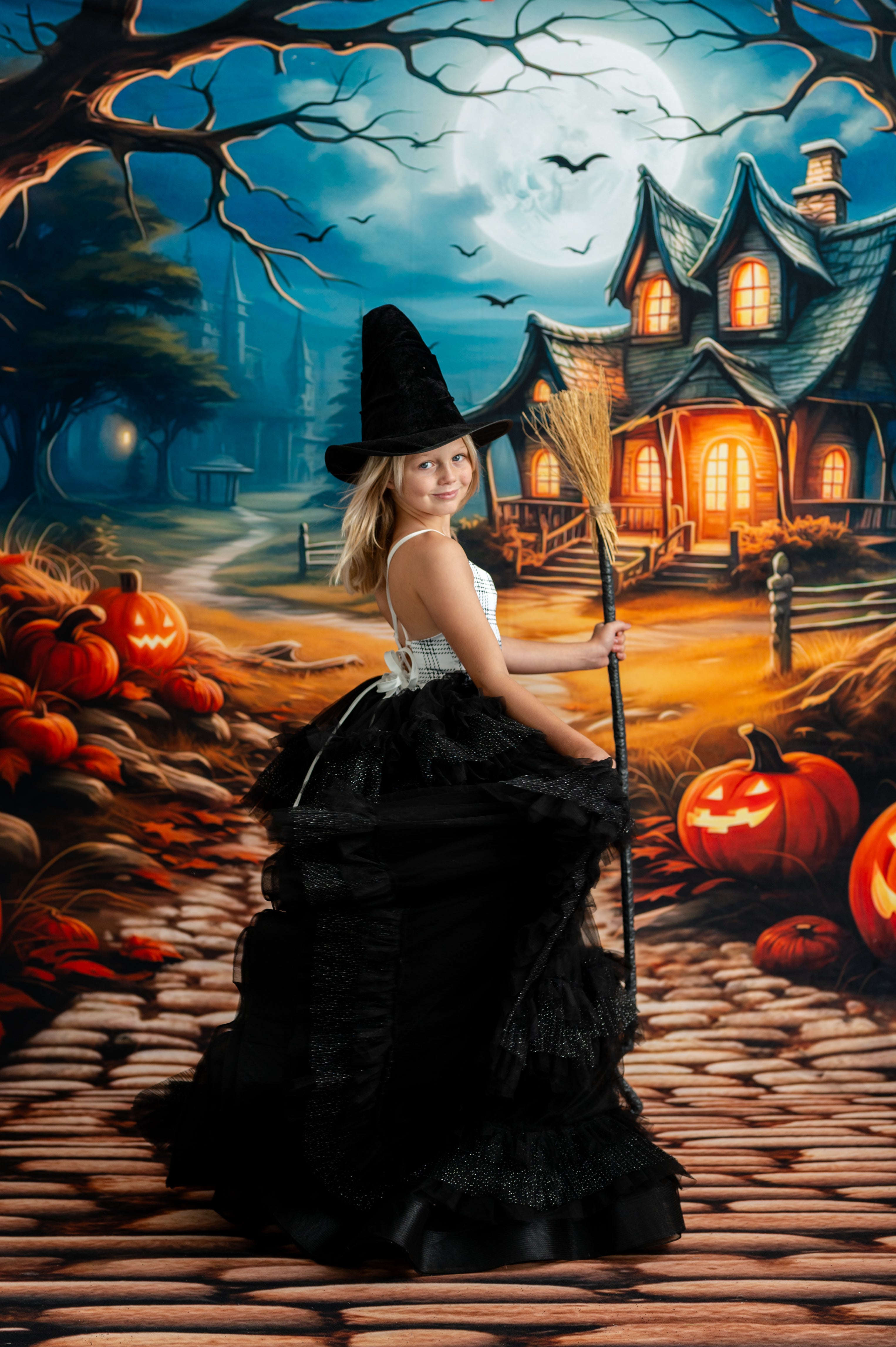 Woman in a witch costume standing in front of a Halloween-themed house with pumpkins and bats.