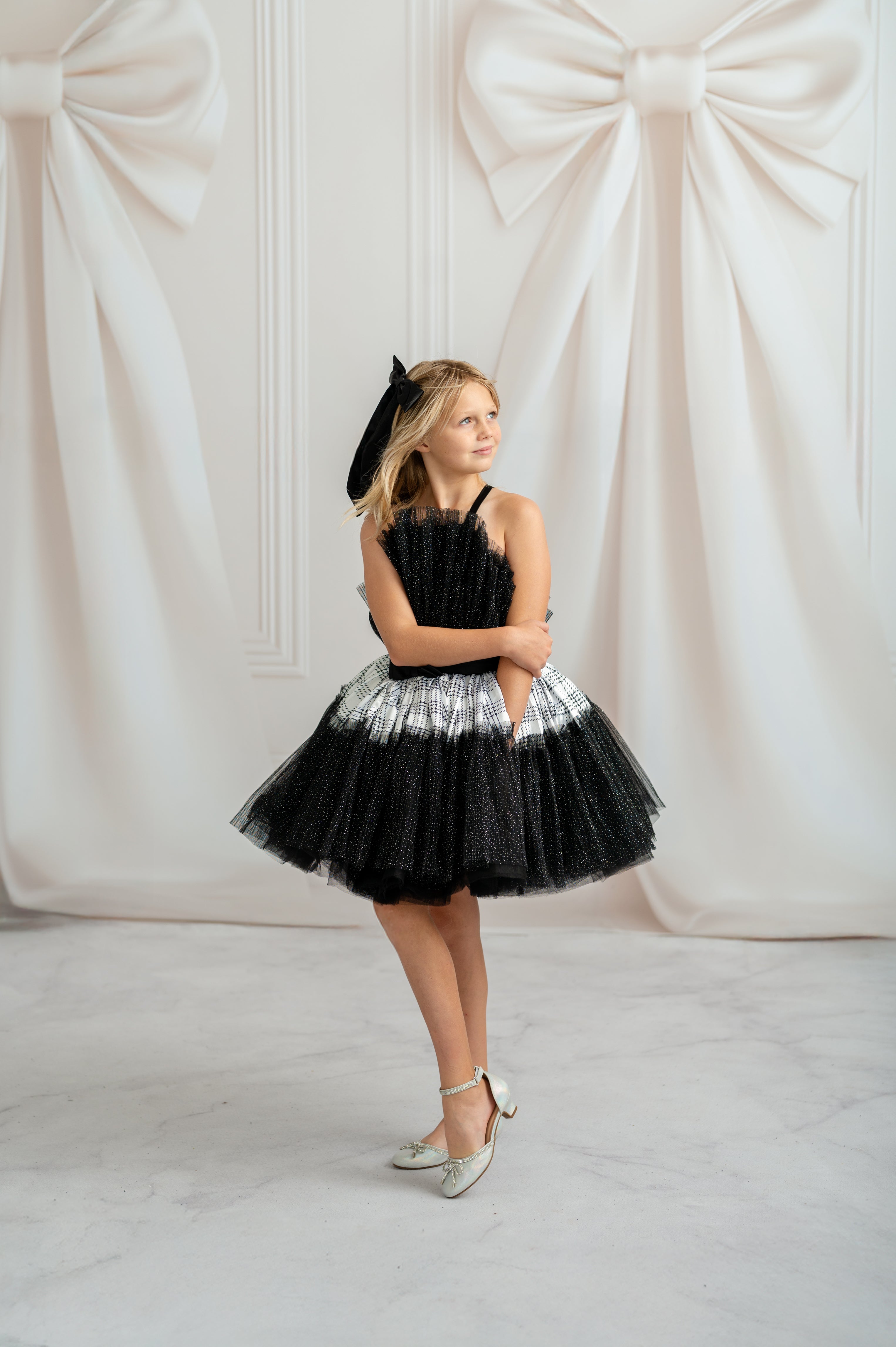 Woman wearing a black and white dress with a hat against a decorative white wall.