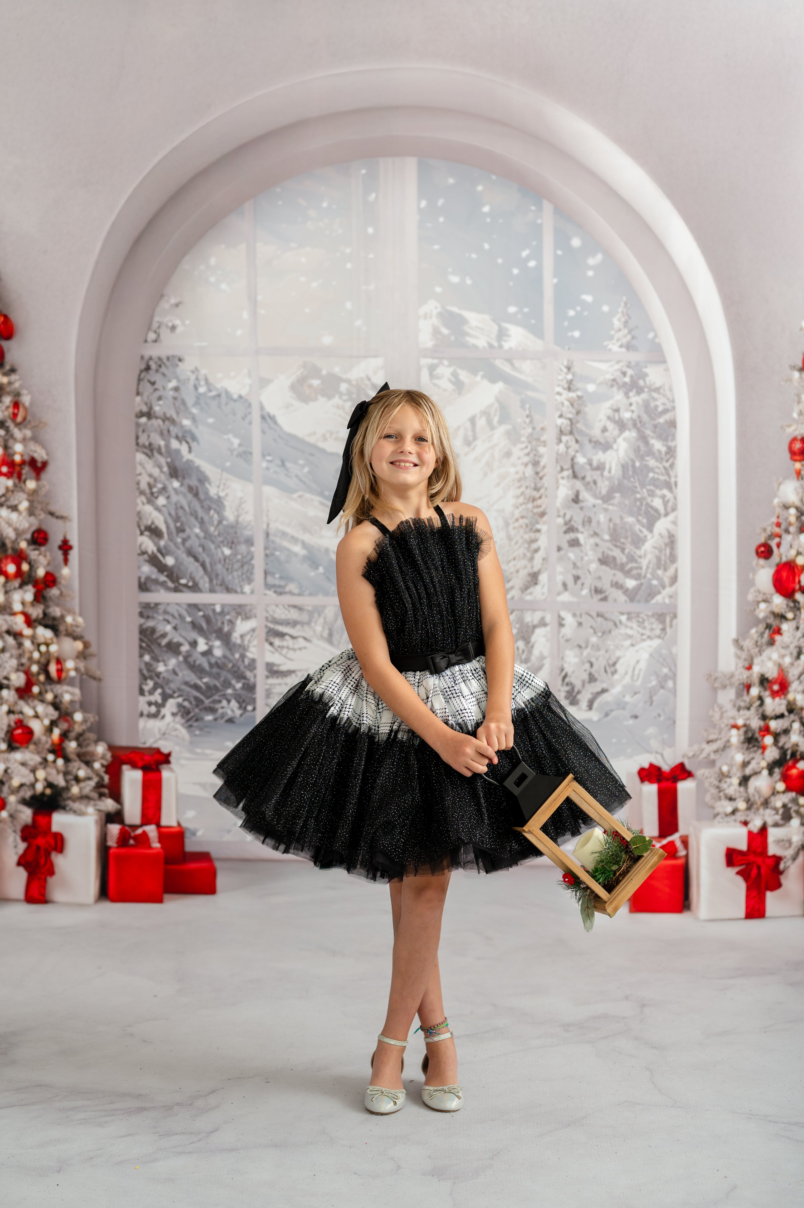 Young girl in a black and white dress holding a gold frame in a festive setting with Christmas decorations.