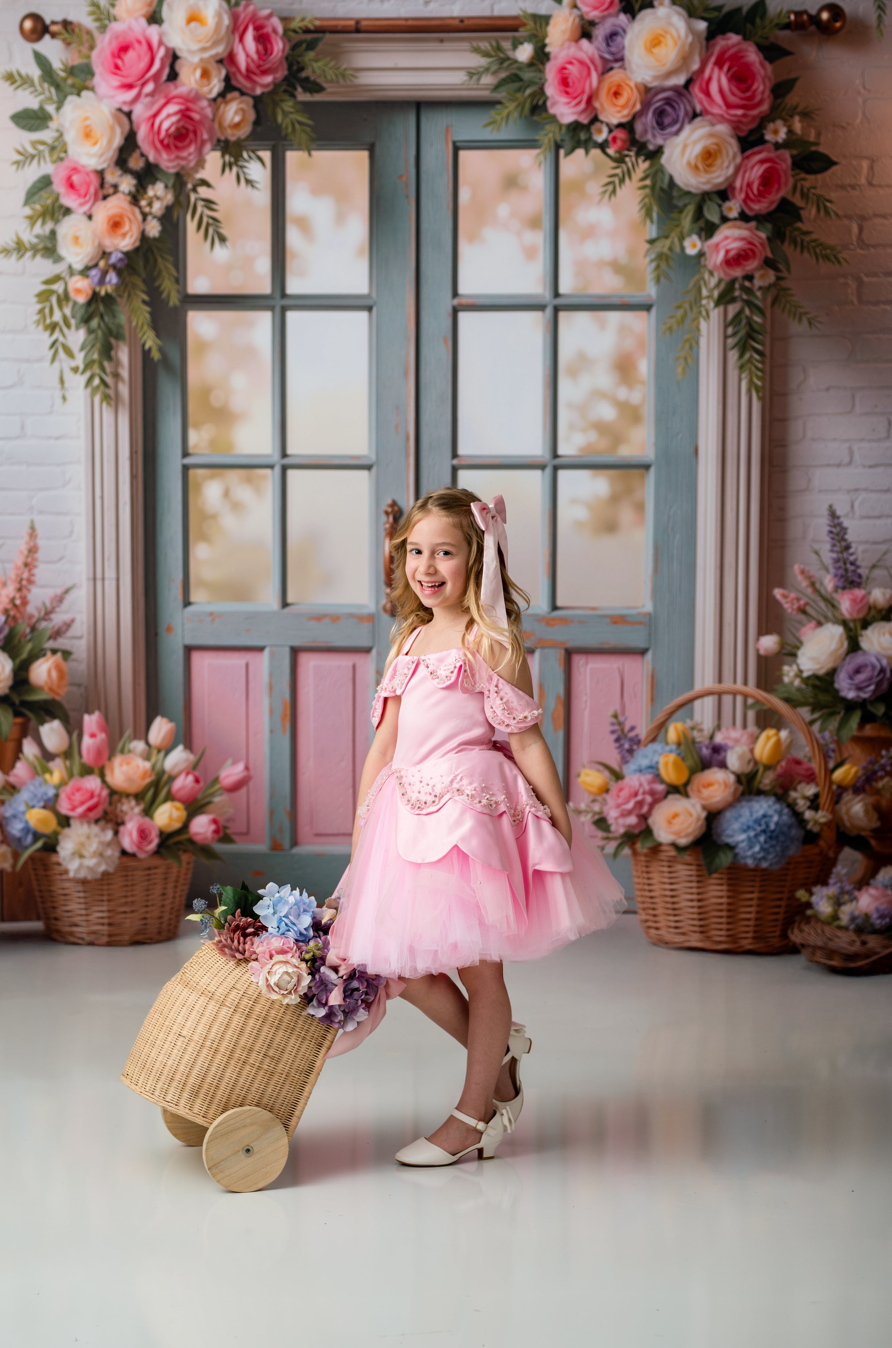 Young girl in a pink dress standing next to a decorated archway with flowers and baskets.