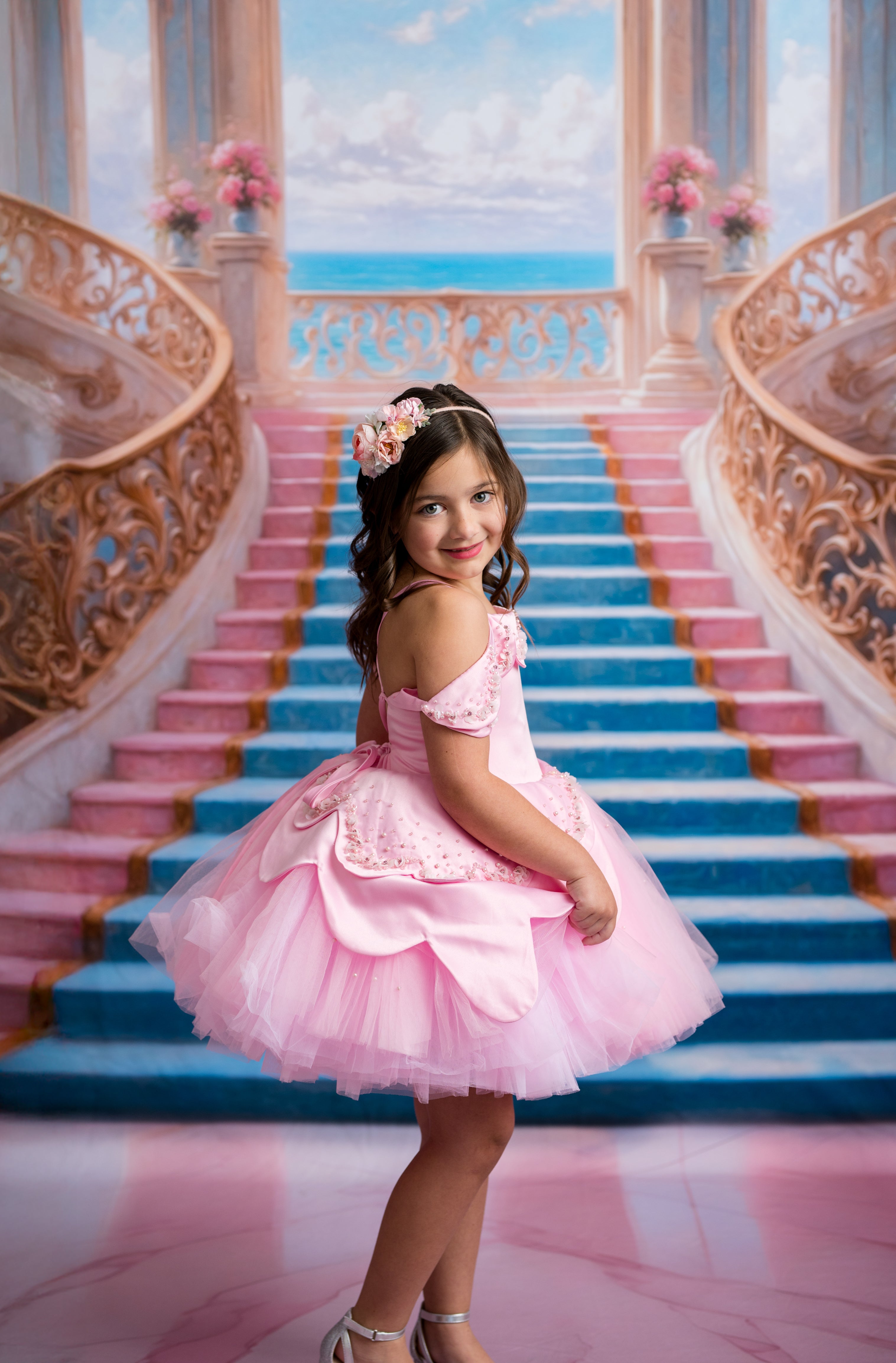 Young girl in a pink dress standing on a grand staircase with ocean view