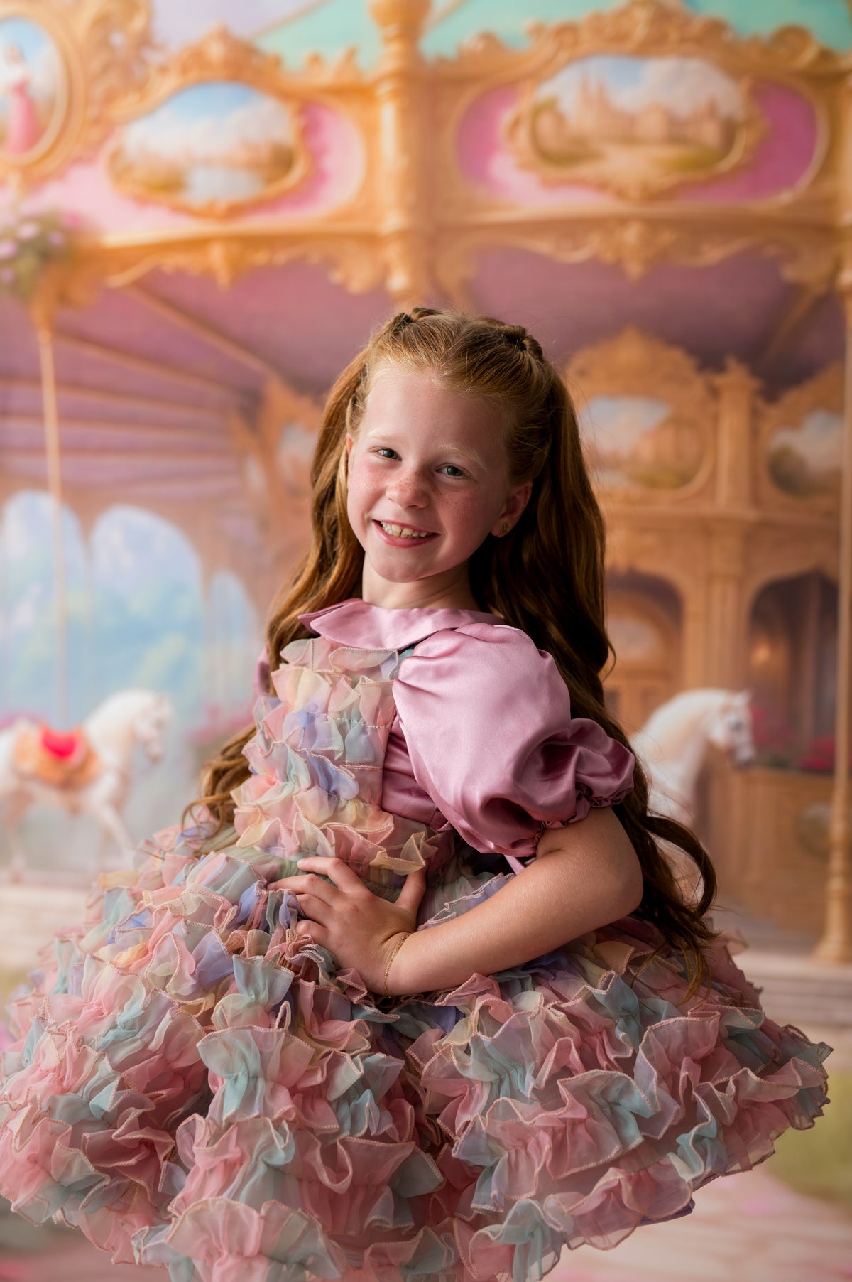 Young girl in a colorful dress sitting on a carousel with pastel-colored horses.
