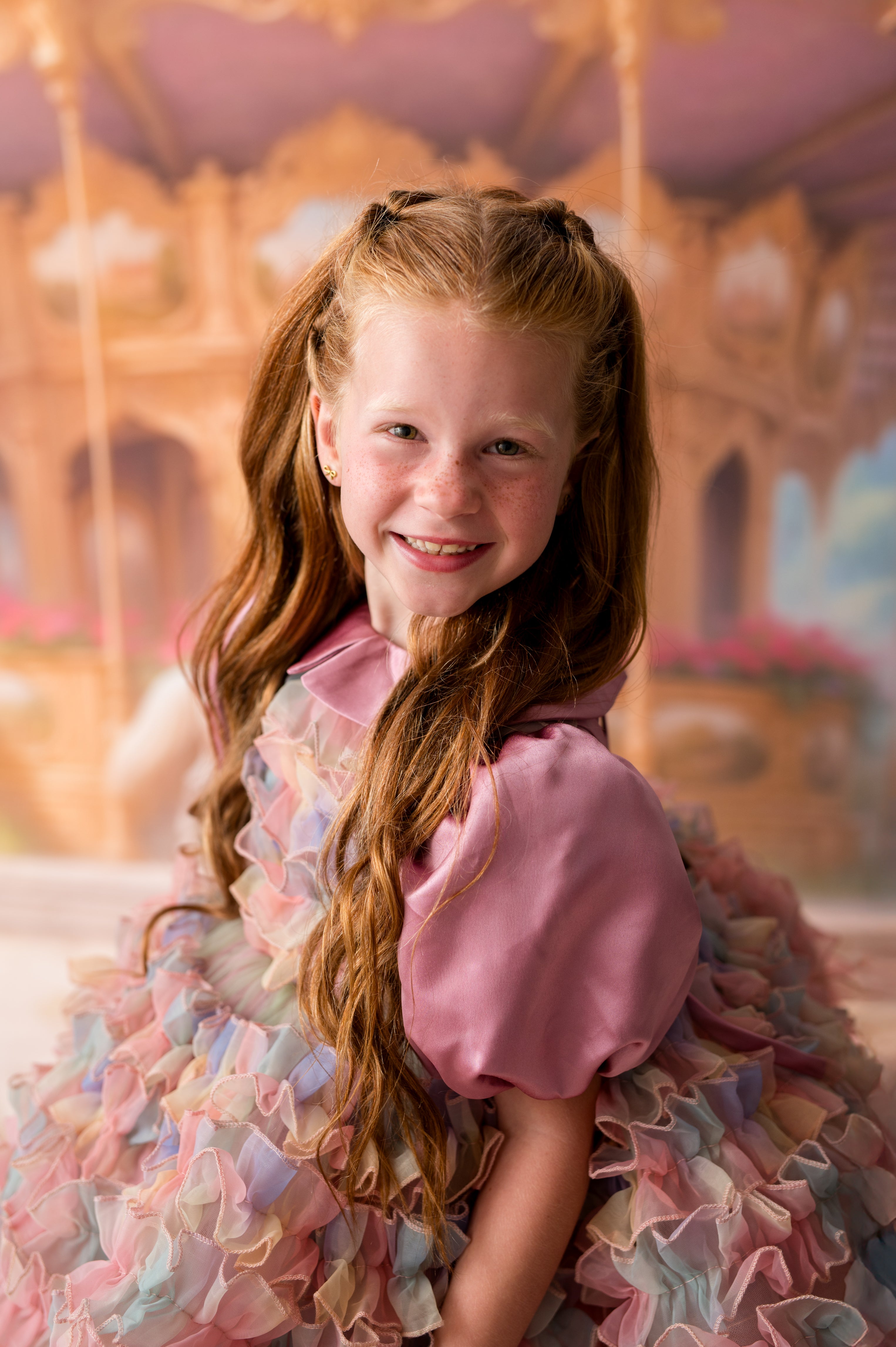Young girl in a colorful dress sitting on a carousel.