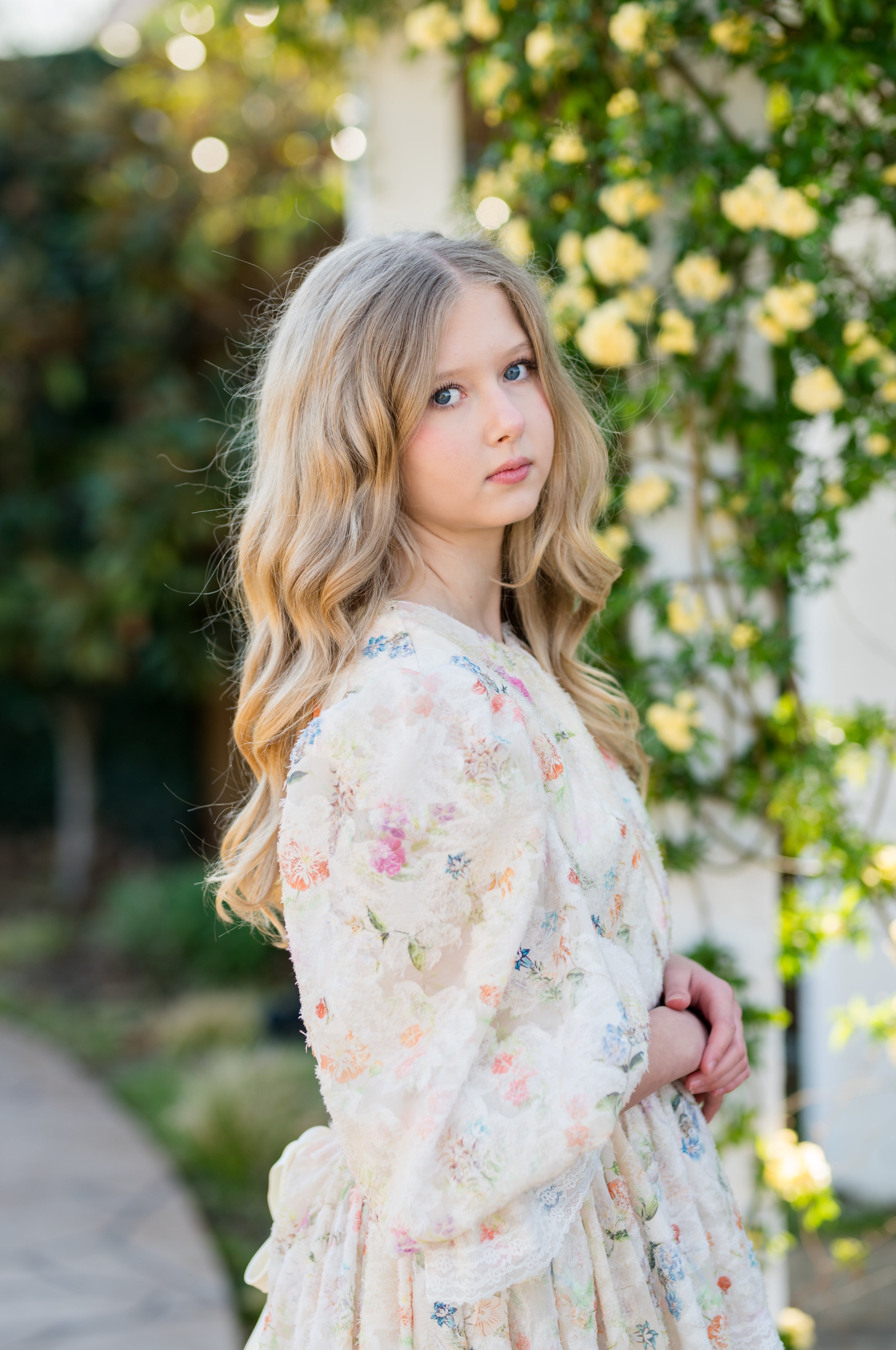 Young woman in a floral dress standing outdoors with greenery and flowers in the background