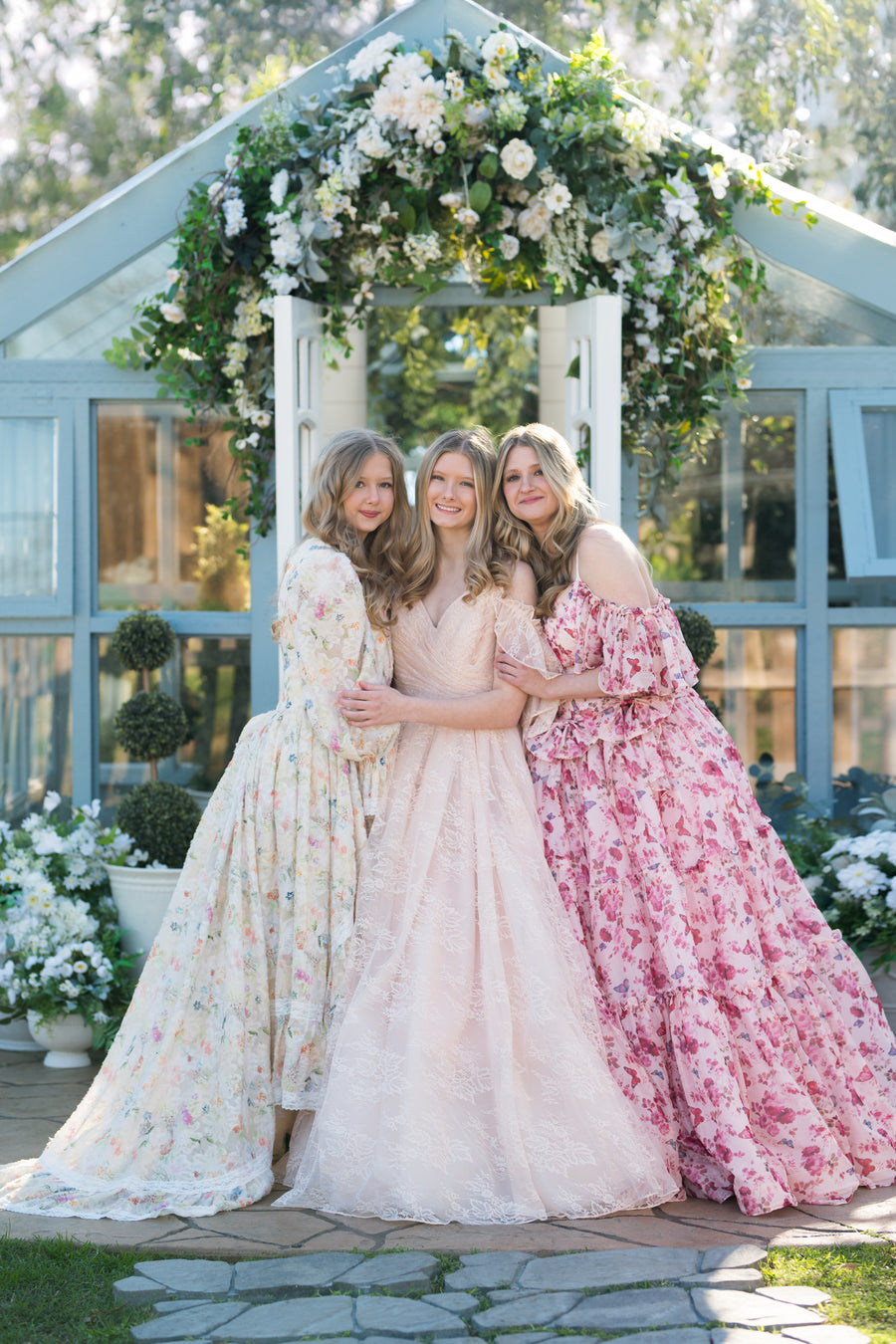 Three women in floral dresses standing under a floral archway.