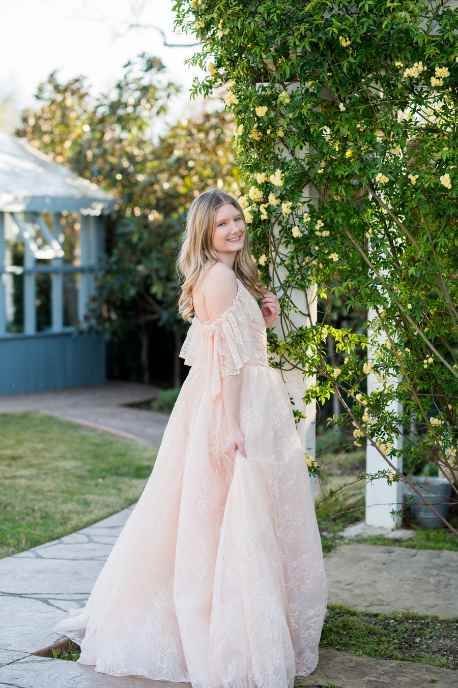 Woman in a flowing dress standing outdoors near a gazebo and floral arch.