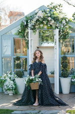 Woman in a floral dress standing in front of a decorated gazebo with flowers and plants.