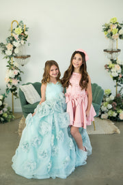 Two young girls in formal dresses standing in a decorated room with floral arrangements.