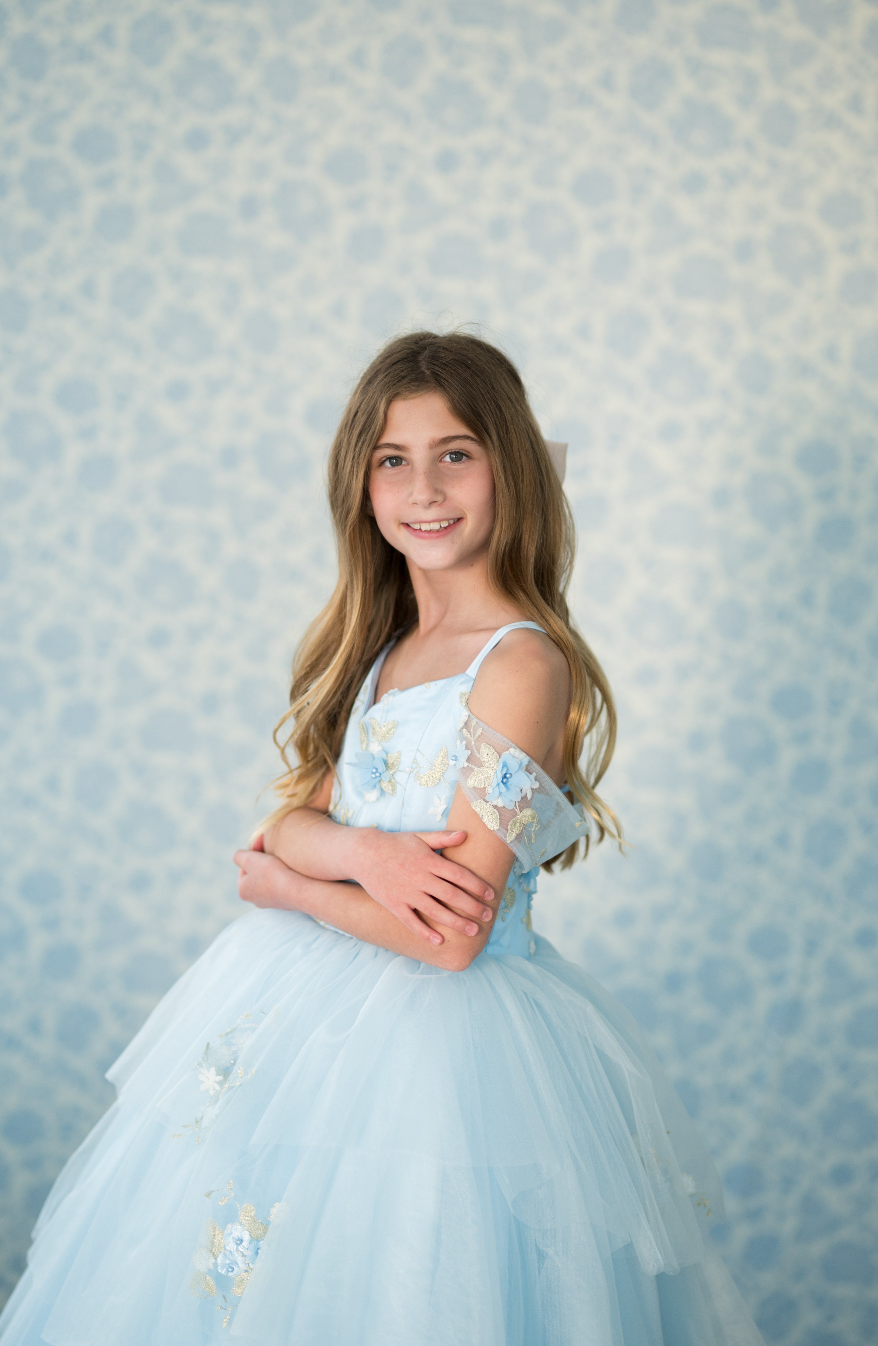 Young girl in a light blue dress with floral details against a patterned background
