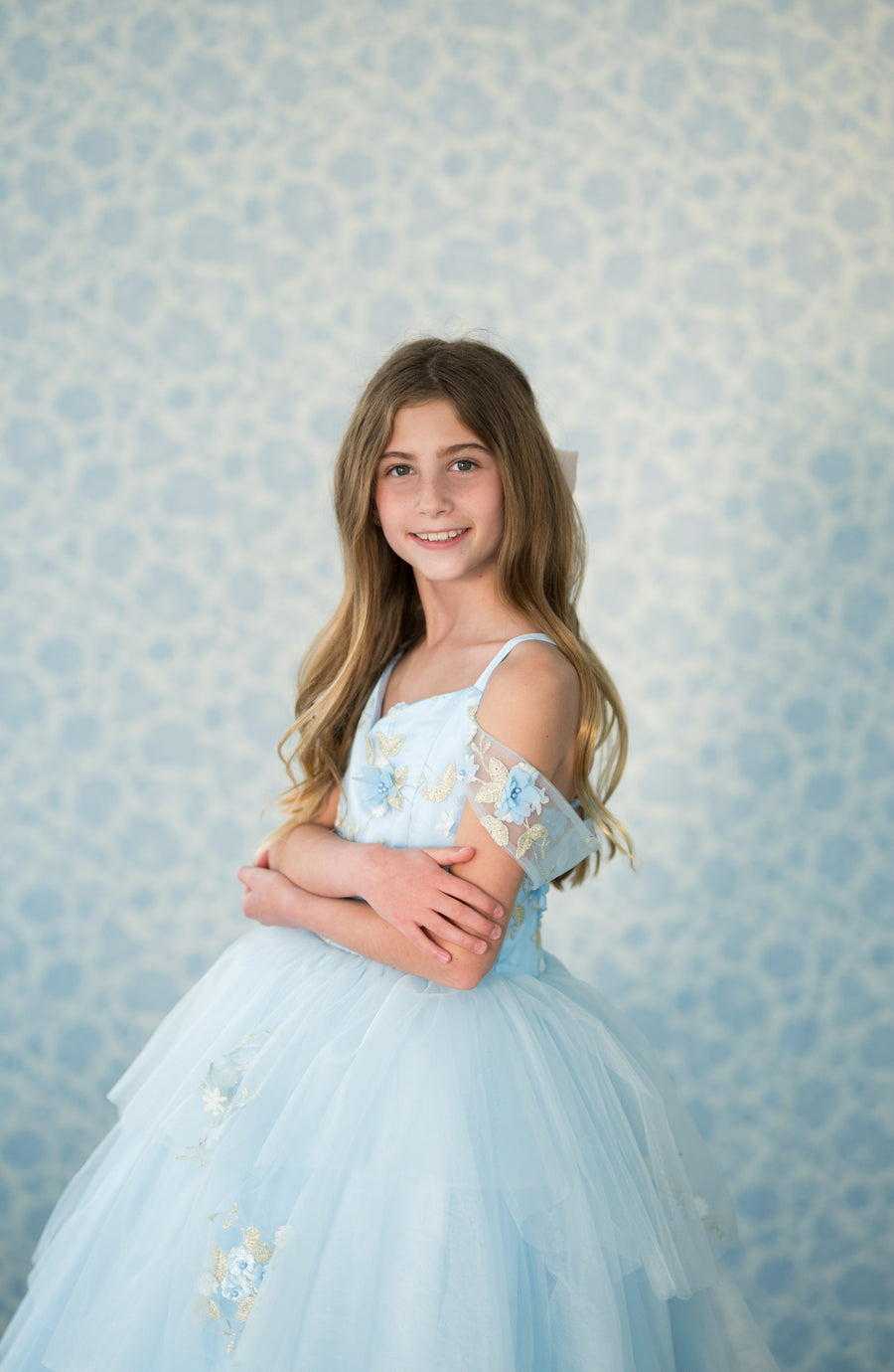 Young girl in a light blue dress with floral details against a patterned background