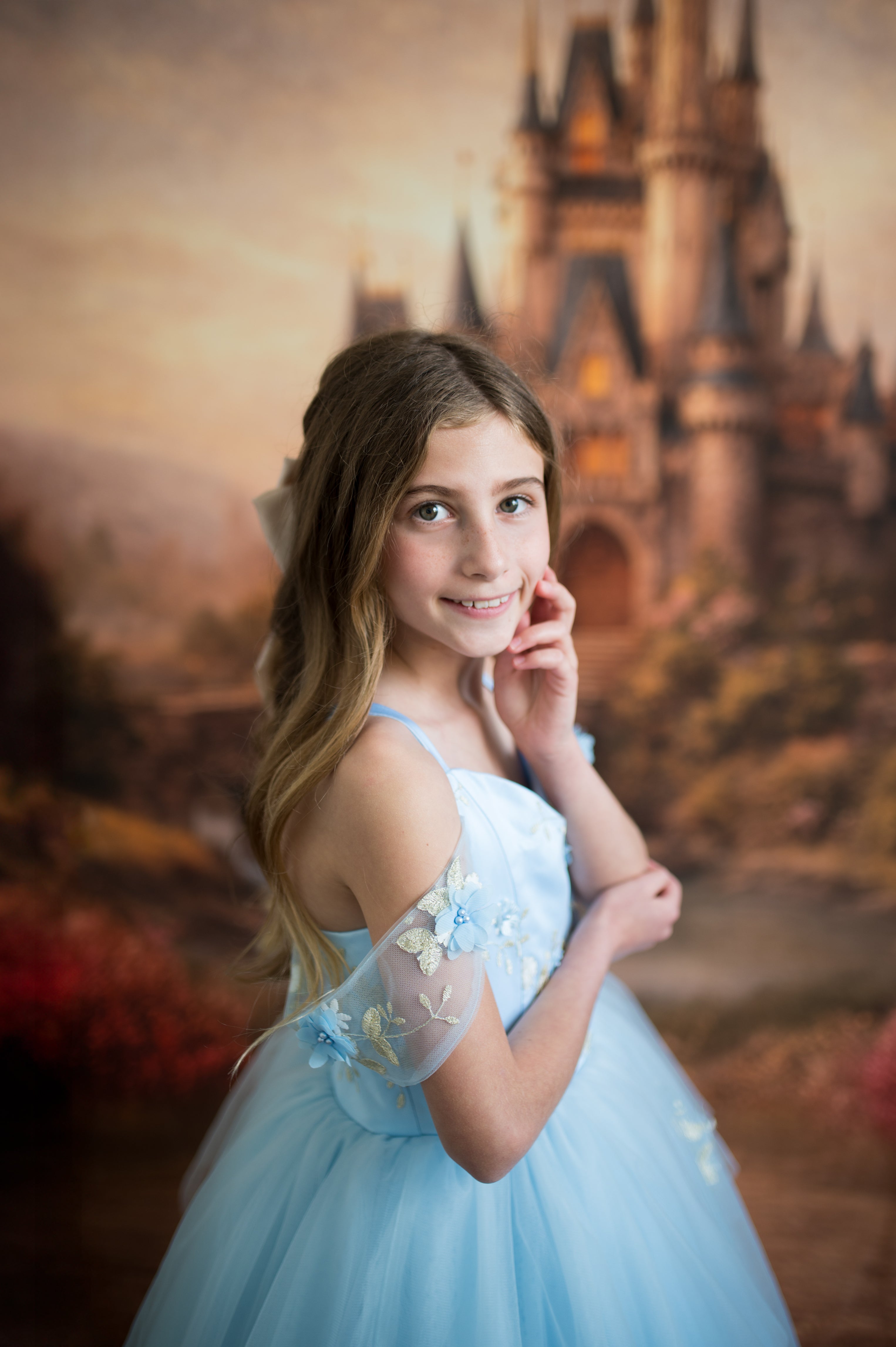 Young girl in a blue dress posing in front of a castle backdrop
