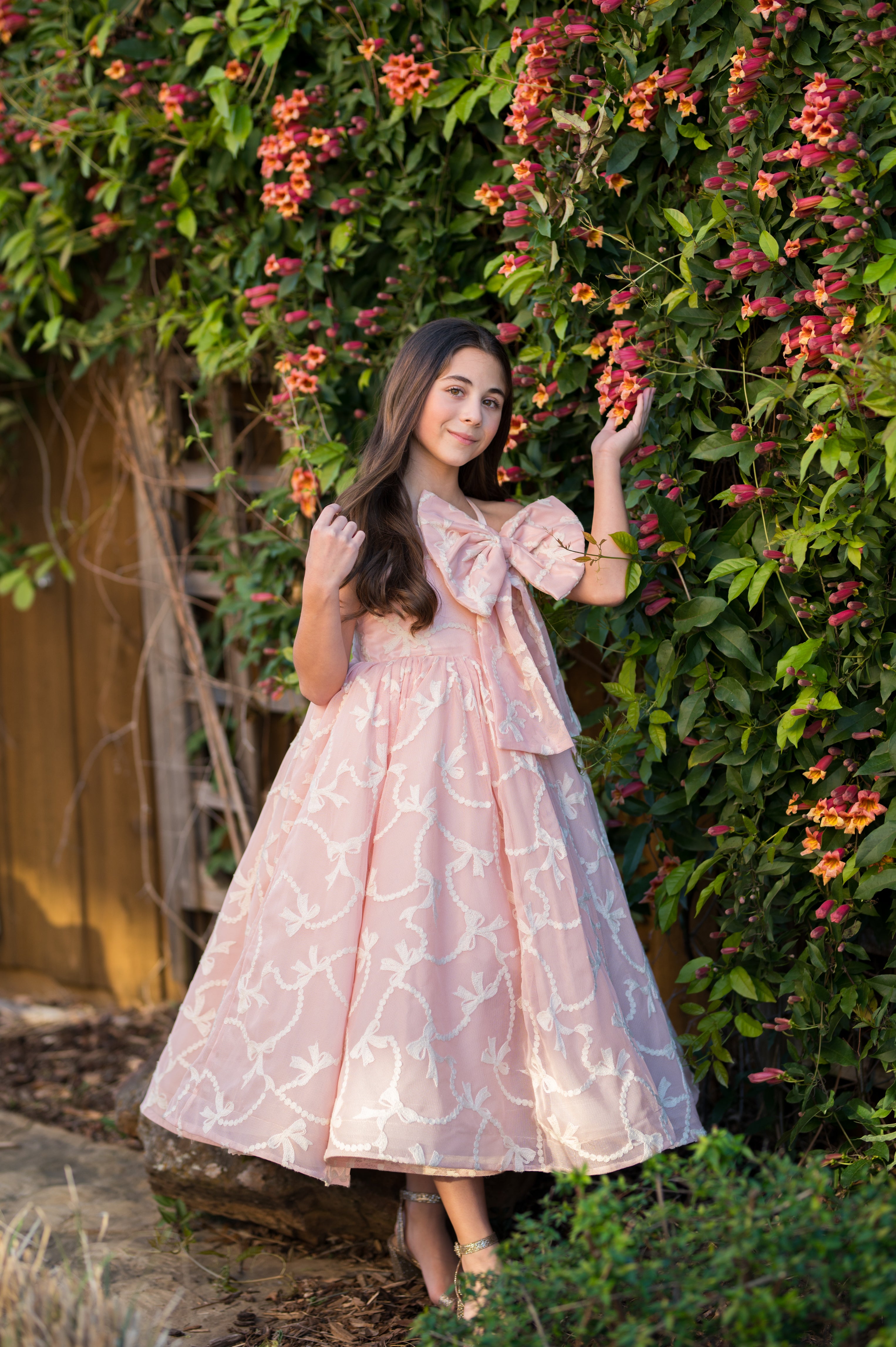 Woman in a pink dress standing in front of a floral wall.
