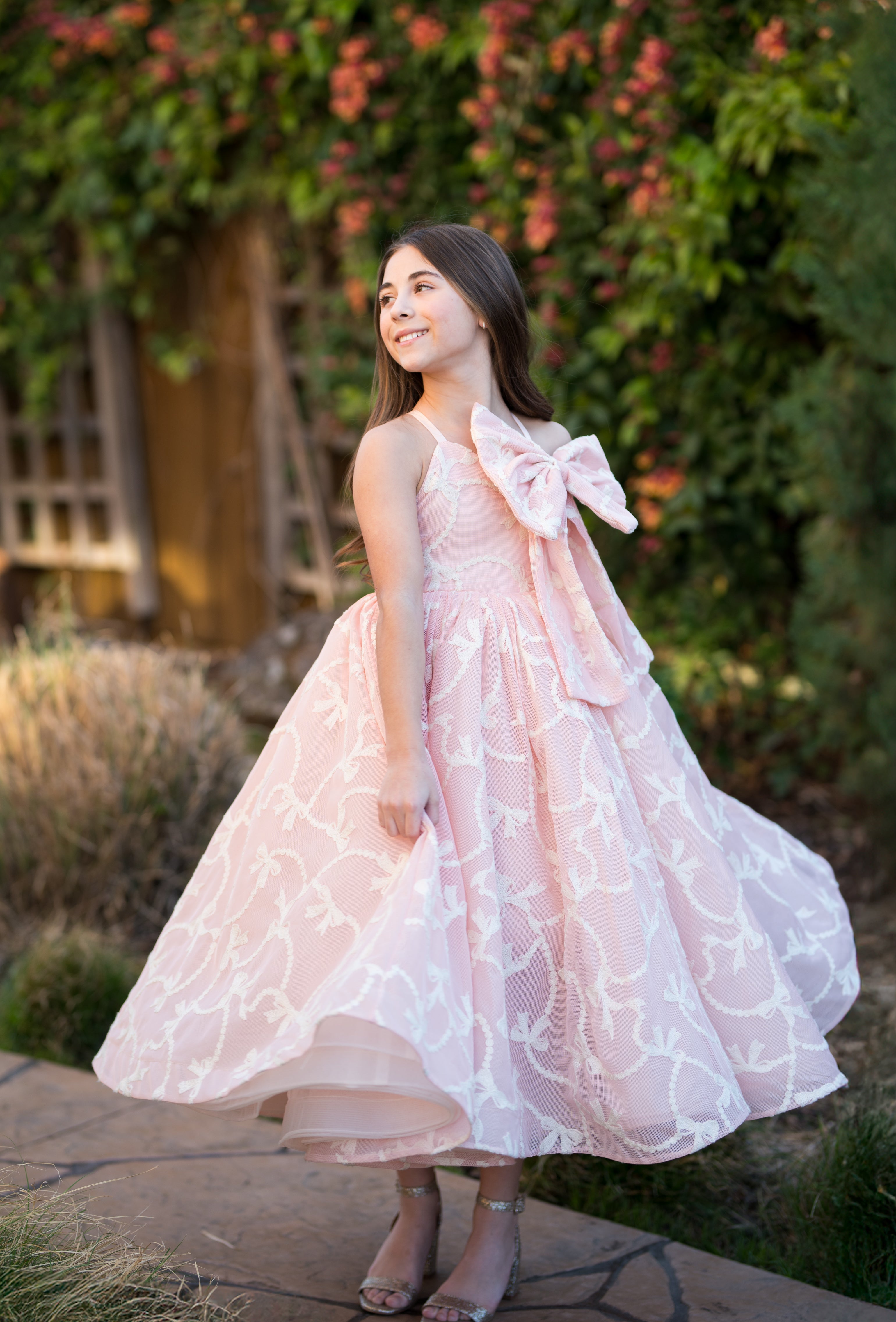 Young girl in a pink floral dress standing outdoors with greenery in the background