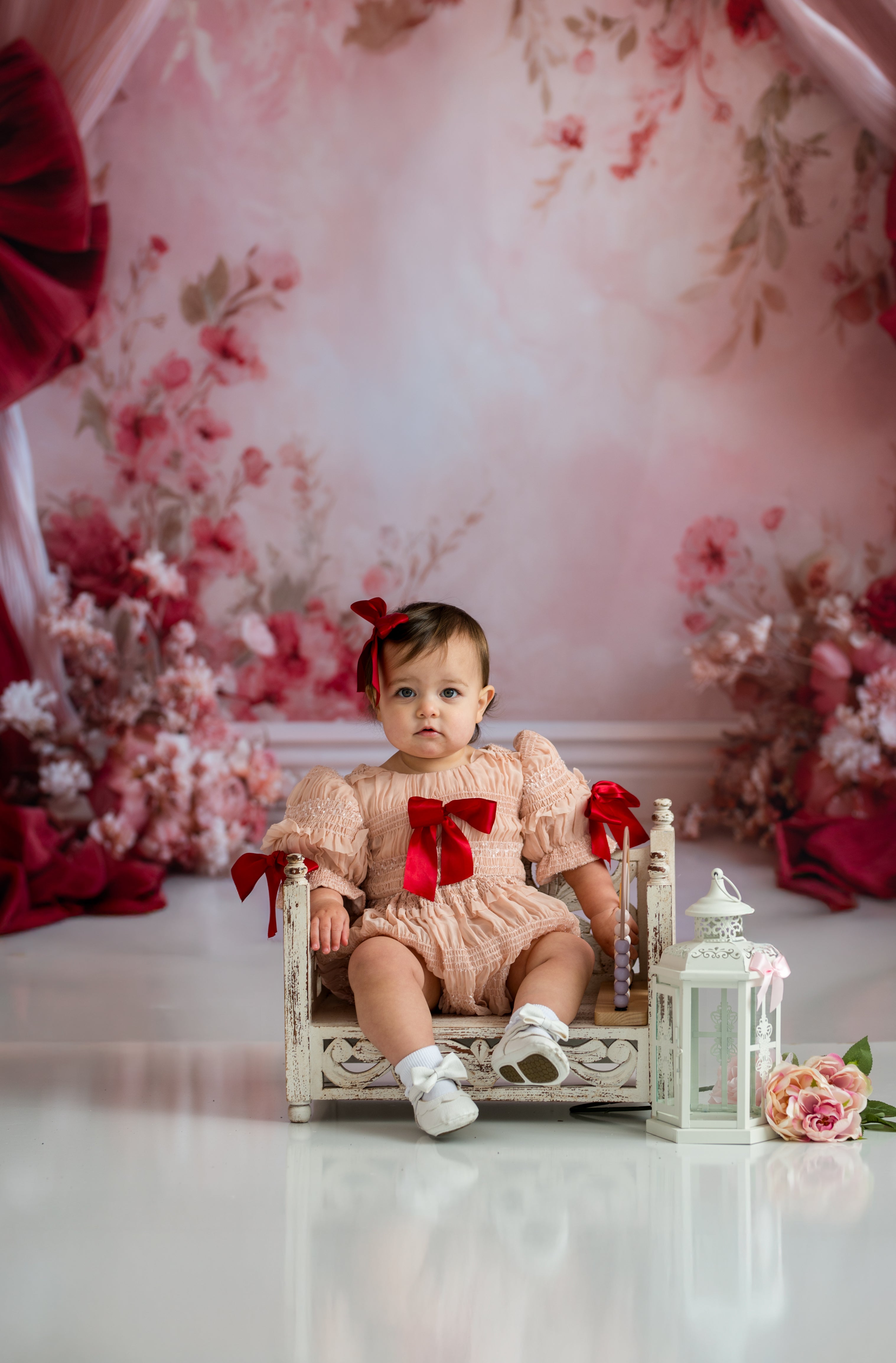 Baby sitting on a small bed with floral decorations and a pink floral backdrop