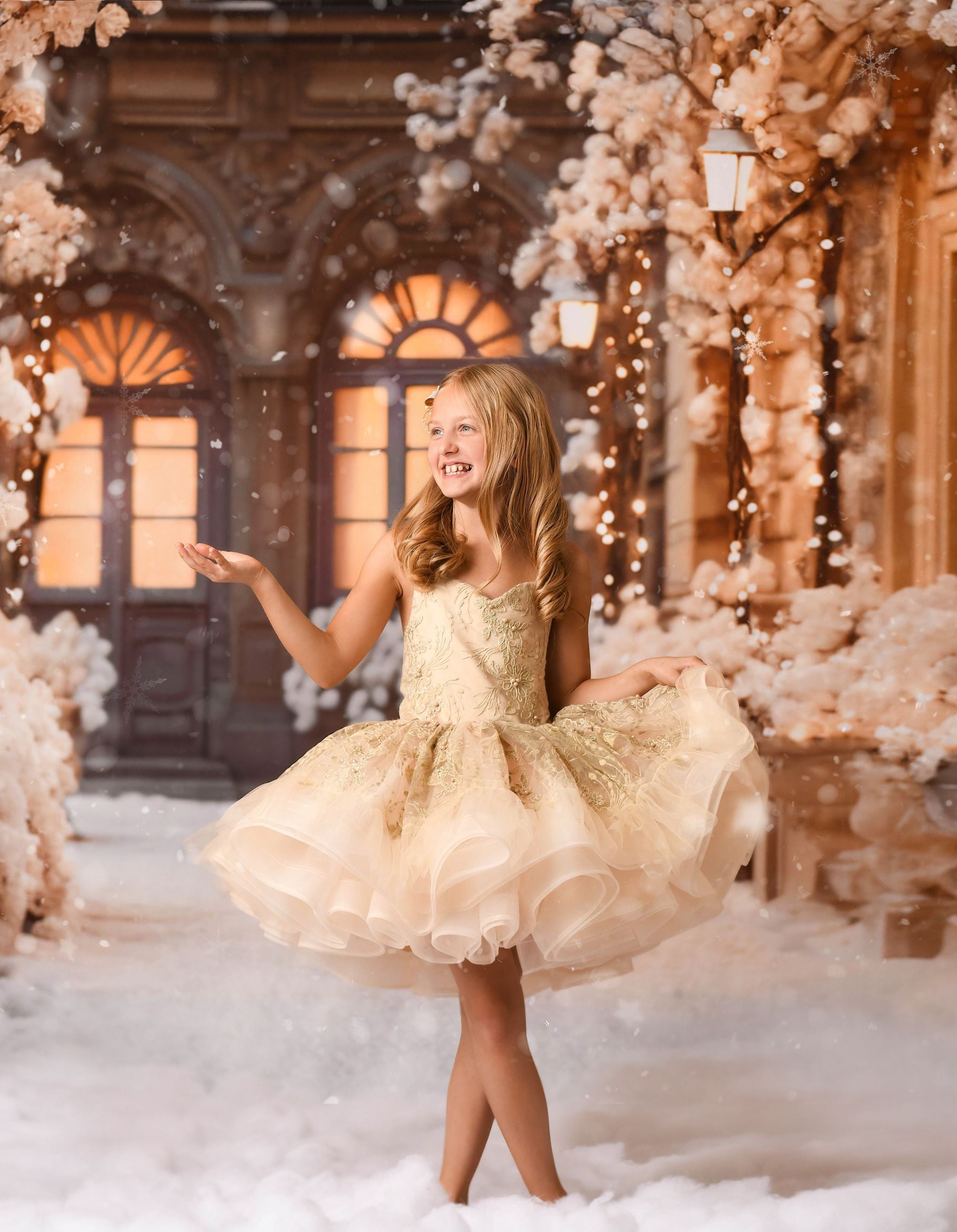 A young girl wearing a golden embroidered tulle dress, standing in a pose amidst a snowy backdrop with floral decorations and a vintage-style building in the background.