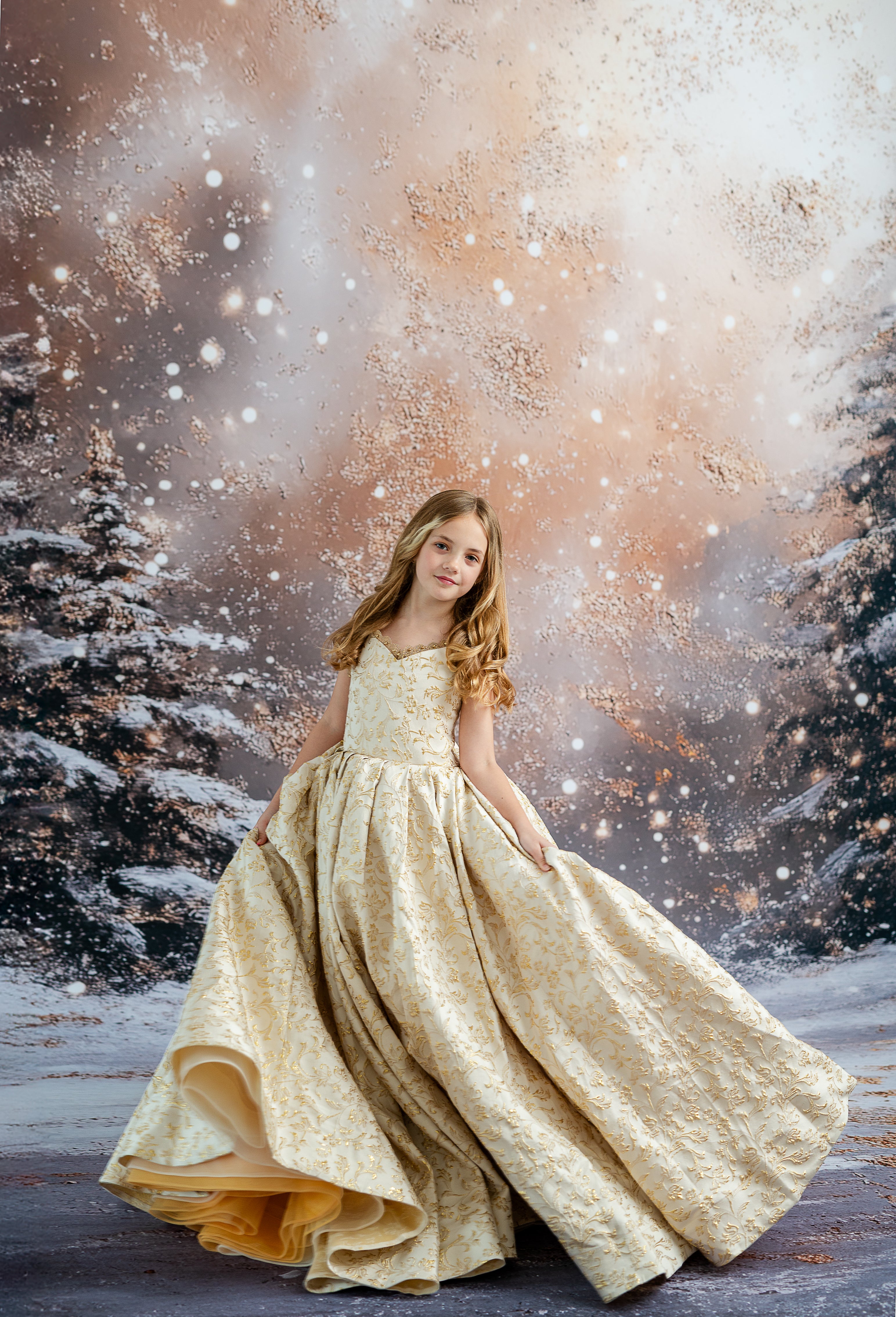 Young girl in a gold dress standing in a snowy landscape with trees.