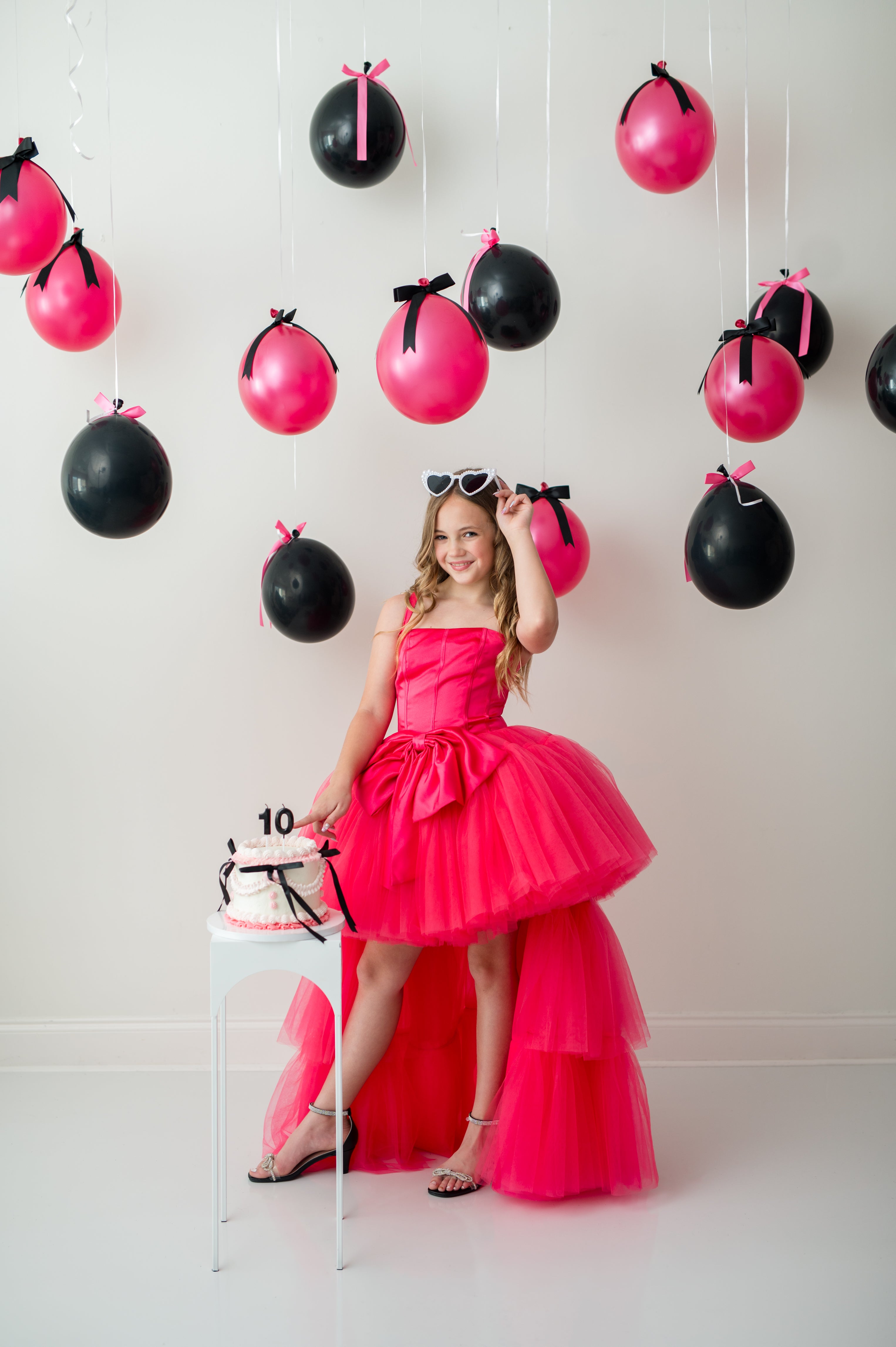 Young girl in a pink dress standing in front of black and pink balloons.