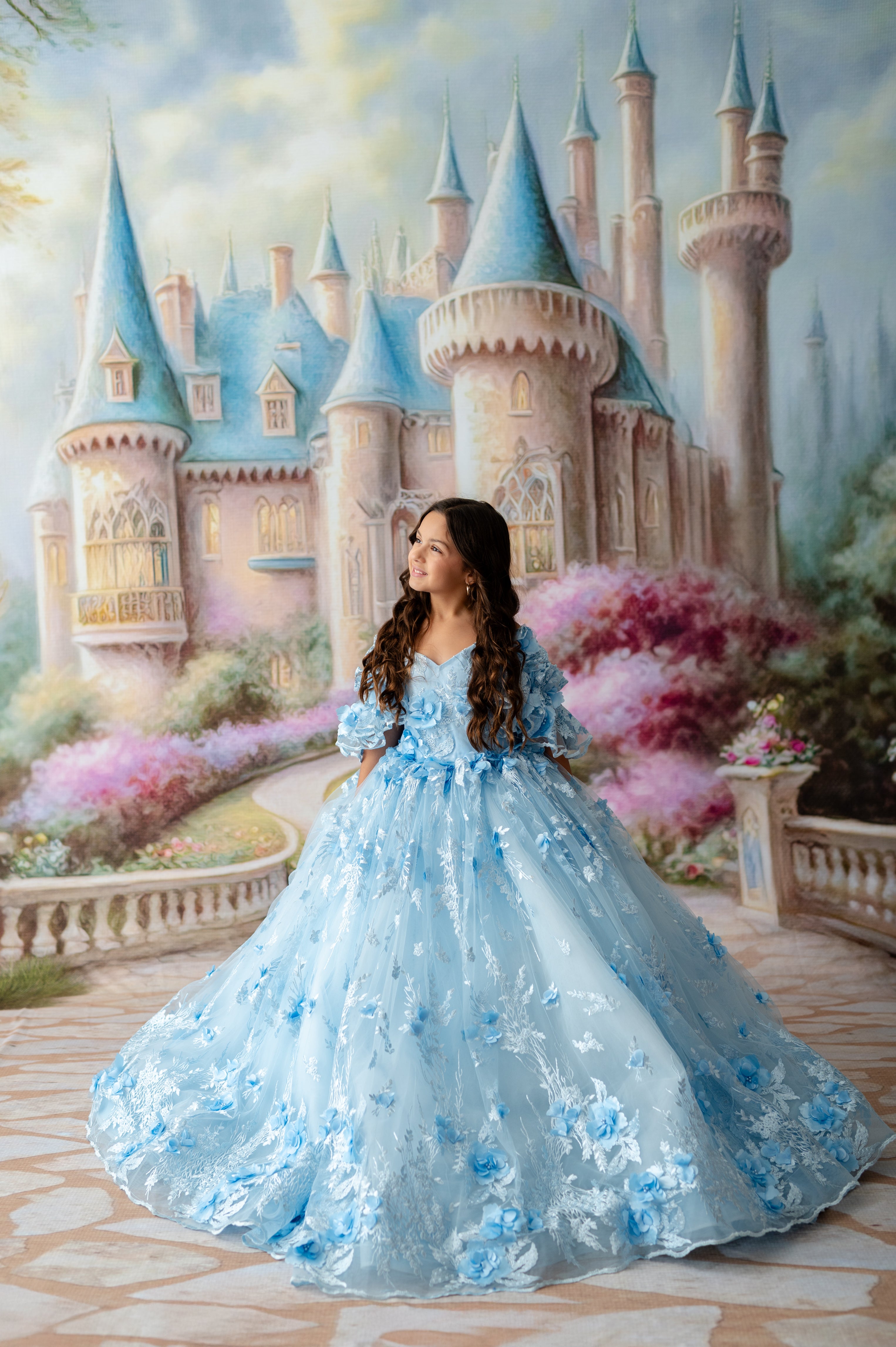 Woman in a blue floral dress standing in front of a fairy-tale castle.