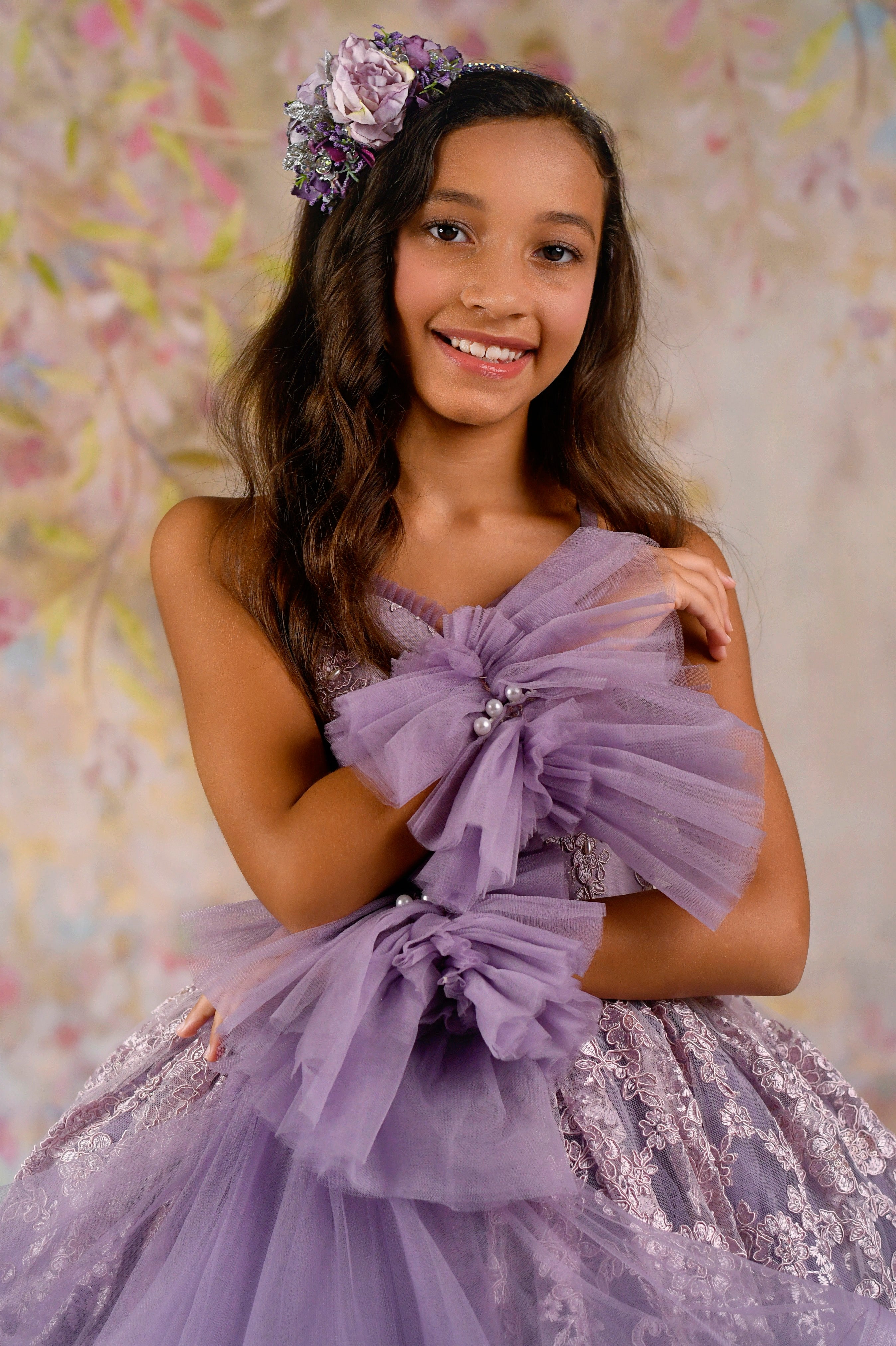 A close-up of a girl wearing a lavender couture gown, highlighting intricate lace embroidery and oversized tulle bow accents.