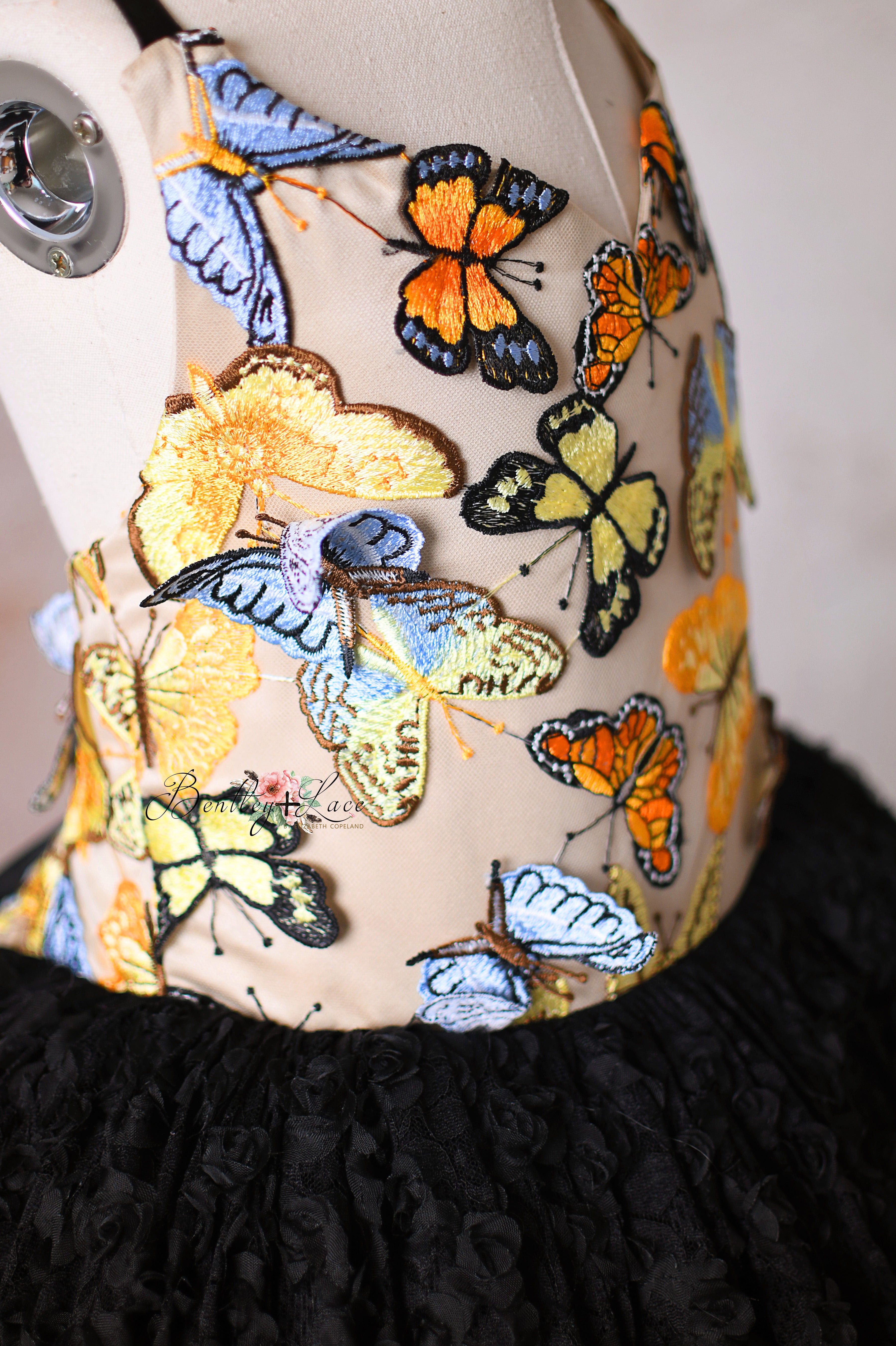 Close-up of colorful butterfly details on a golden bodice with a bold black skirt.
