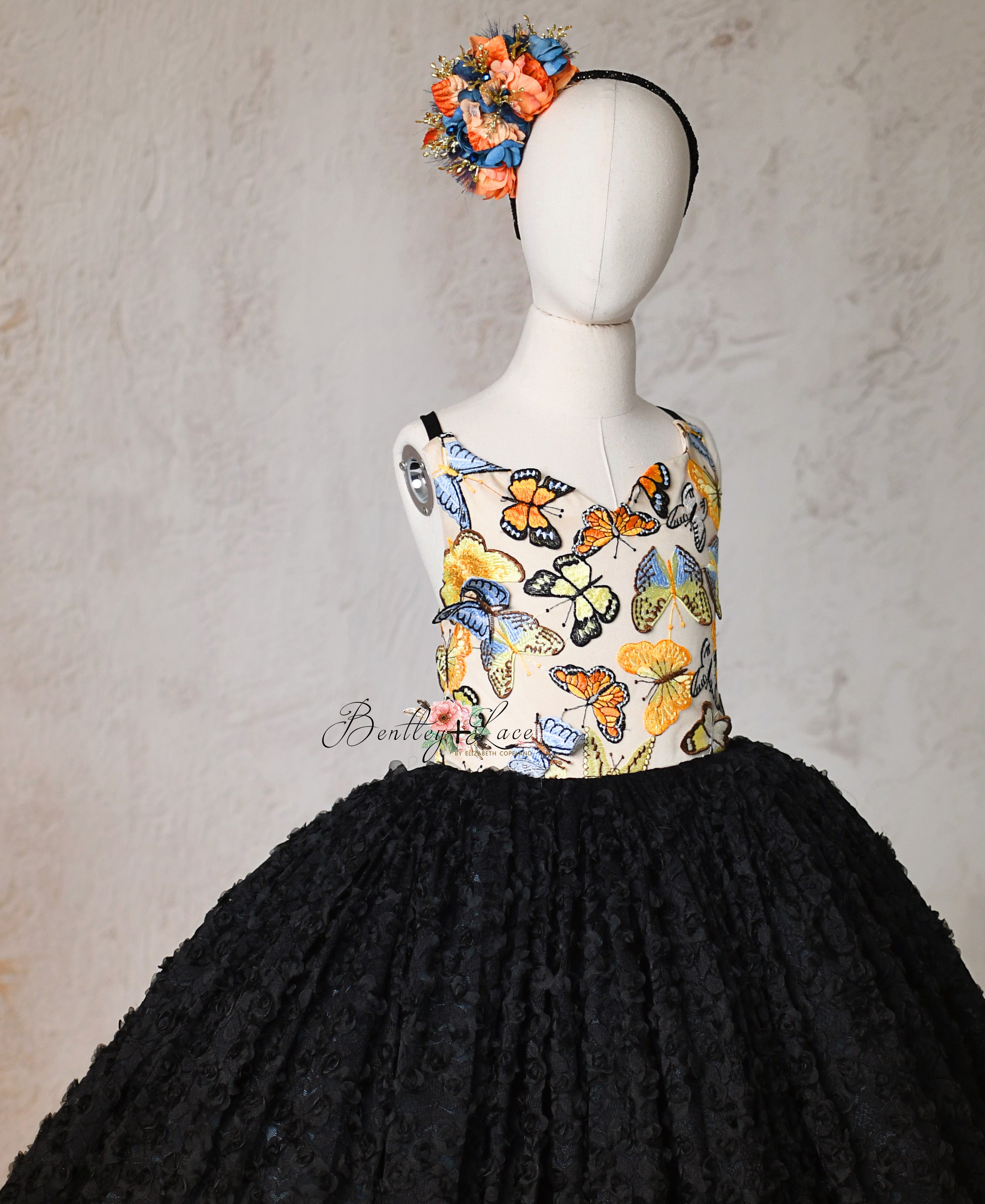 Whimsical butterfly-embroidered bodice paired with a textured rosette skirt in black.
