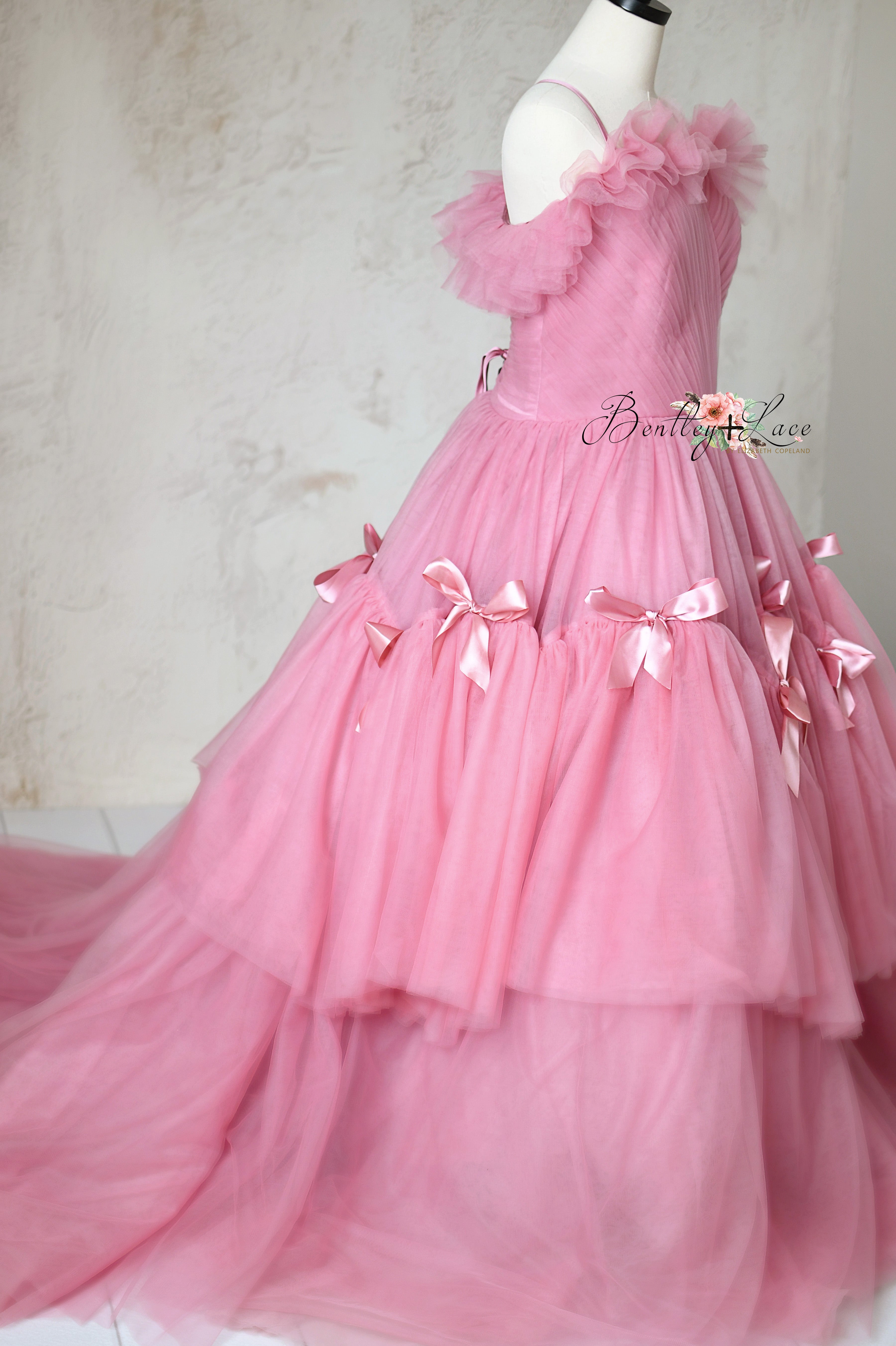 Elegant pink floor-length gown with delicate satin bows and tulle layers.
