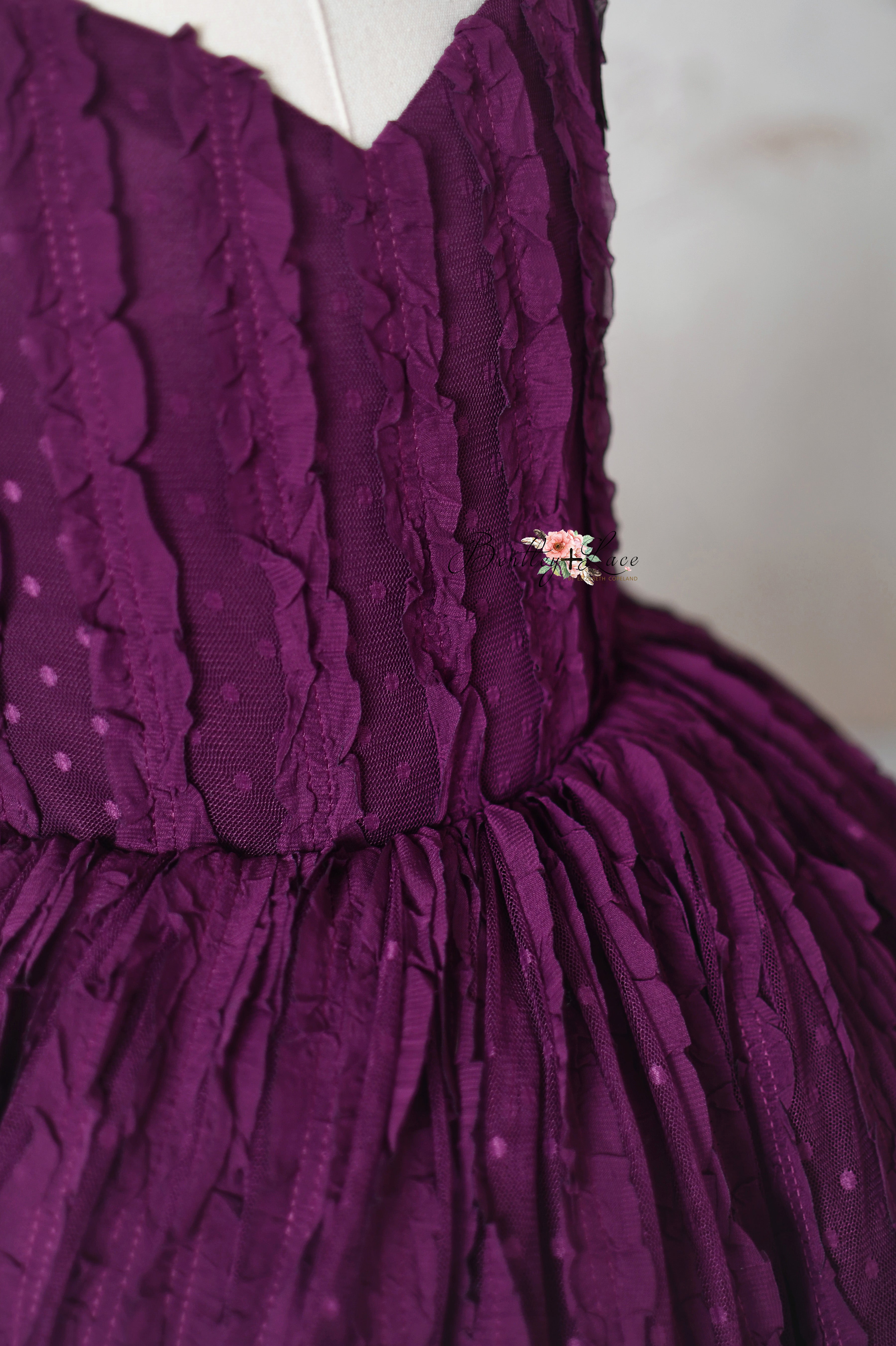 A rich purple formal dress with a flowing, full skirt and intricate lace textures, styled on a mannequin.
